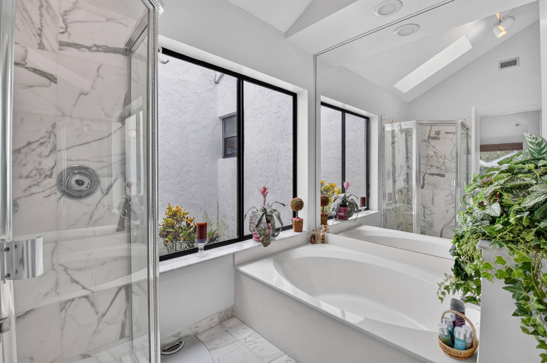 20065 Waters Edge Drive, #101, Boca Raton, FL 33434 Recessed tub with an expansive mirror, enclosed shower with marble-look tile, and a vaulted ceiling with a skylight