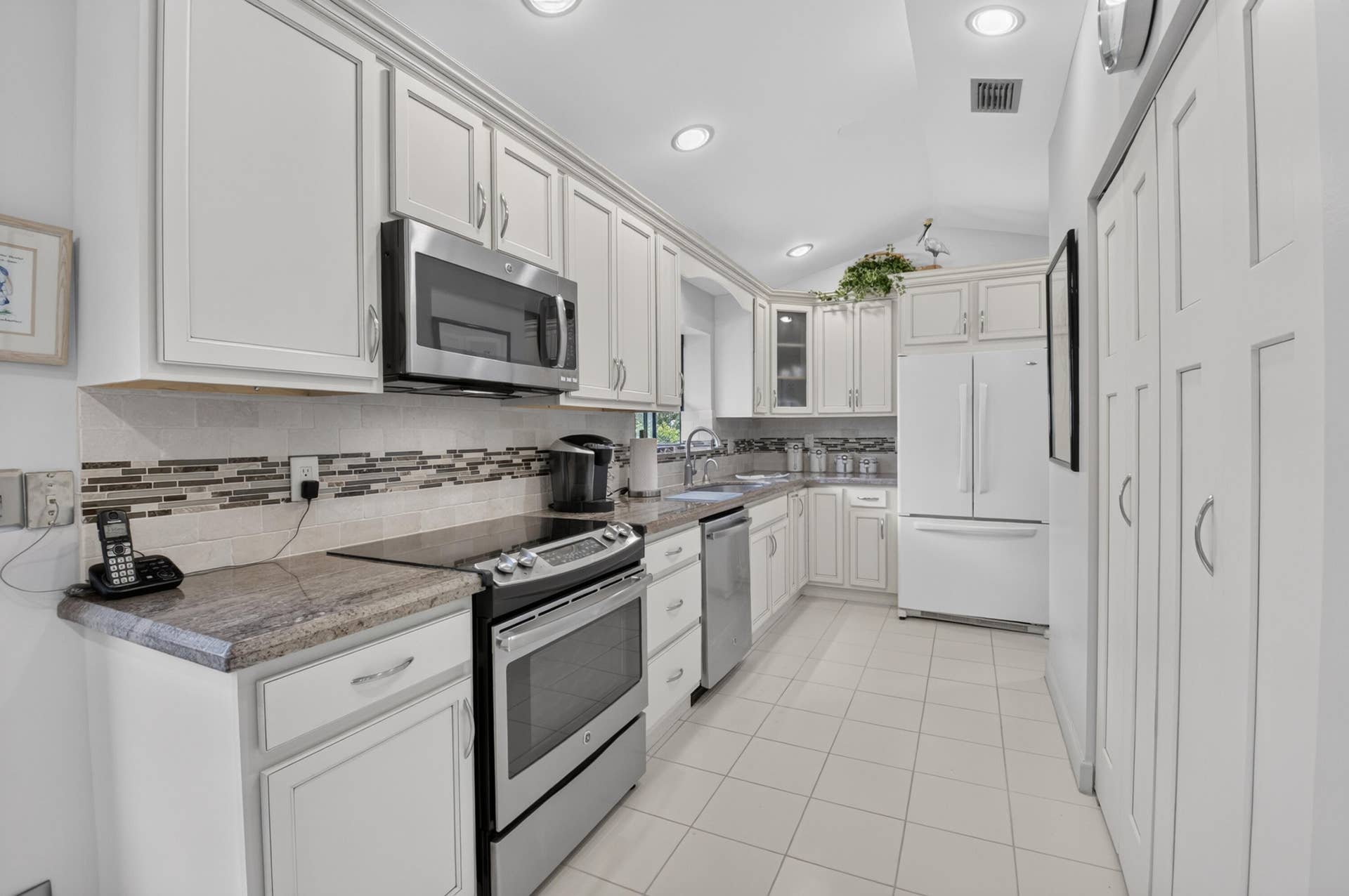 20065 Waters Edge Drive, #101, Boca Raton, FL 33434 Vaulted ceiling kitchen featuring white cabinetry, tile flooring, stone countertops, stainless steel microwave, and integrated panel pantry storage