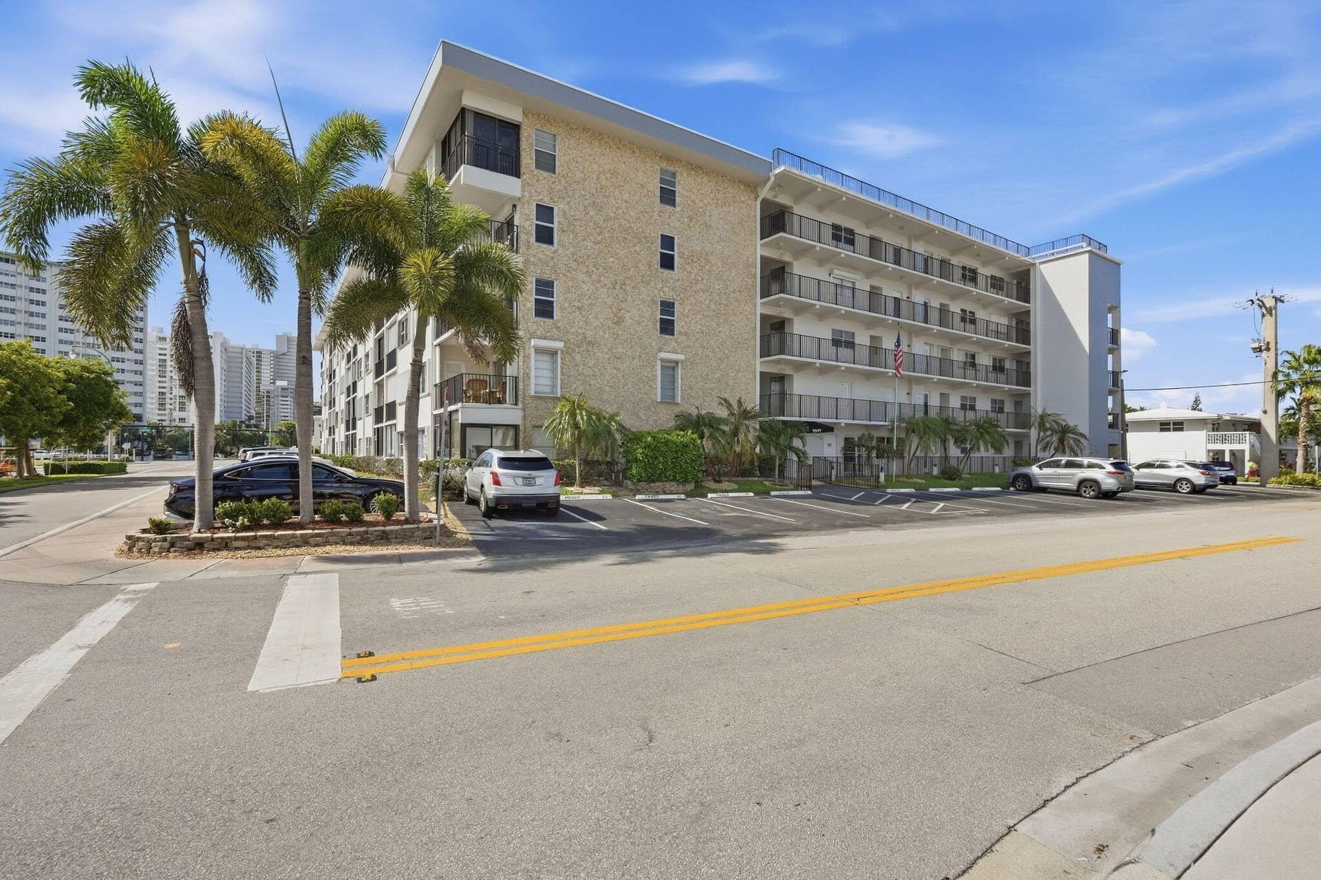 Multi-story building featuring exterior balconies with metal railings, a stone facade, and a paved parking area