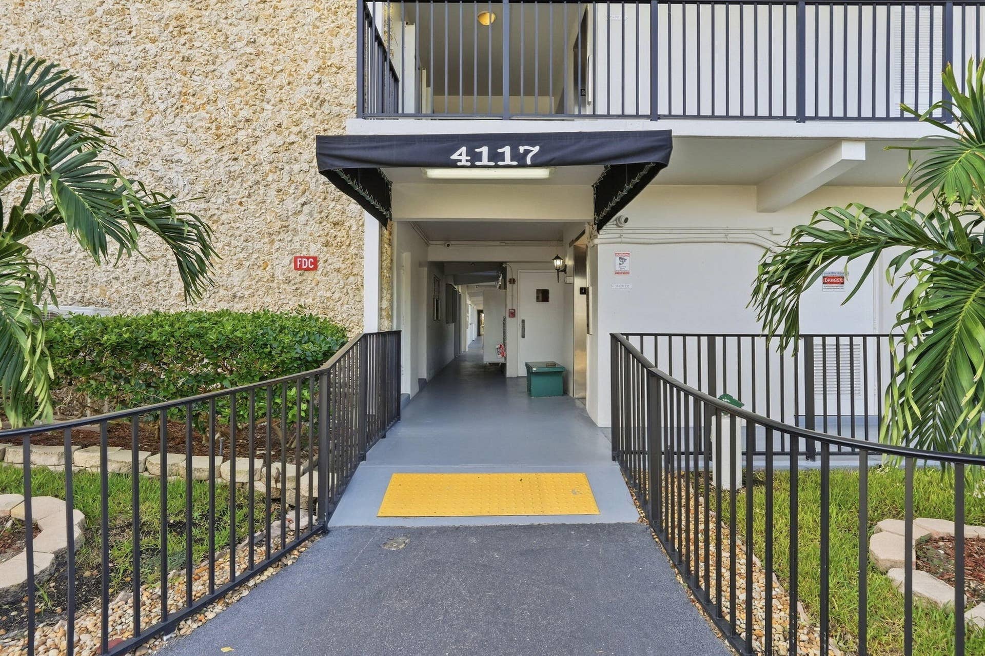 Building entrance featuring a covered walkway with black awning, black metal railings, and textured exterior wall