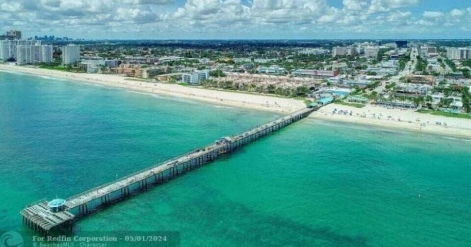 Expansive beachfront with a pier, clear ocean waters, and a coastal city backdrop