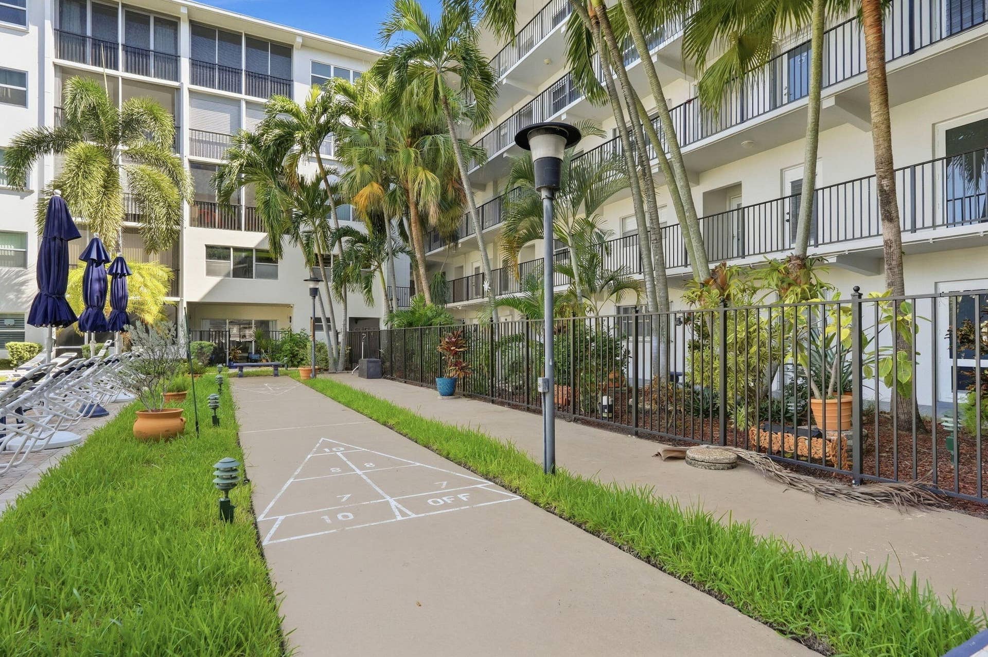 Shuffleboard court with a paved surface and marked game lines, surrounded by manicured grass and palm trees