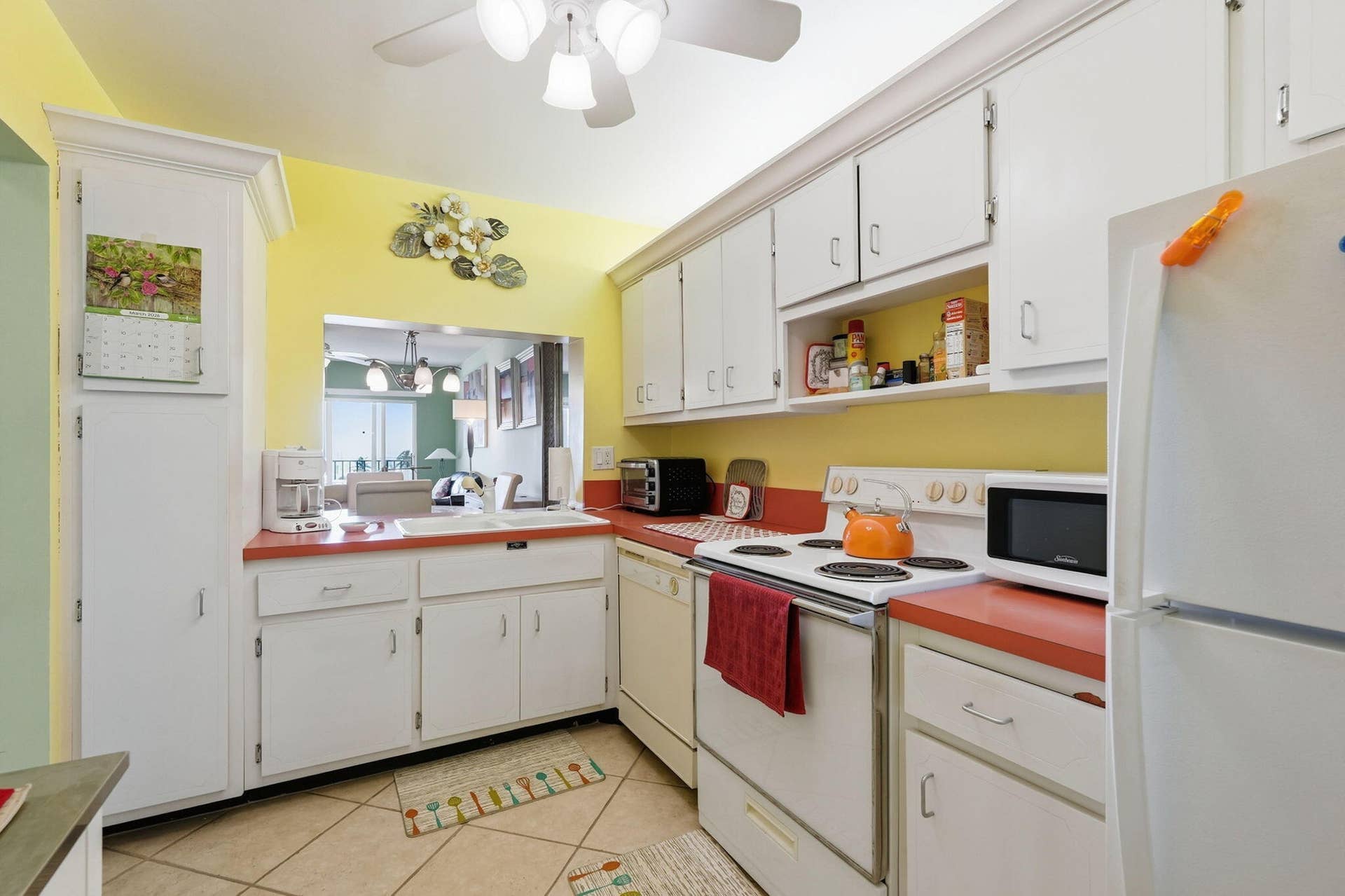 Kitchen featuring white cabinetry, red countertops, a pass-through window, tile flooring, and a ceiling fan with integrated lighting