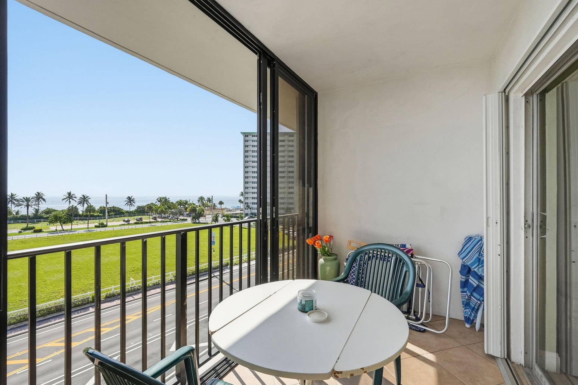 Balcony featuring sliding glass doors, tile flooring, and metal railings overlooking a grassy expanse and distant ocean