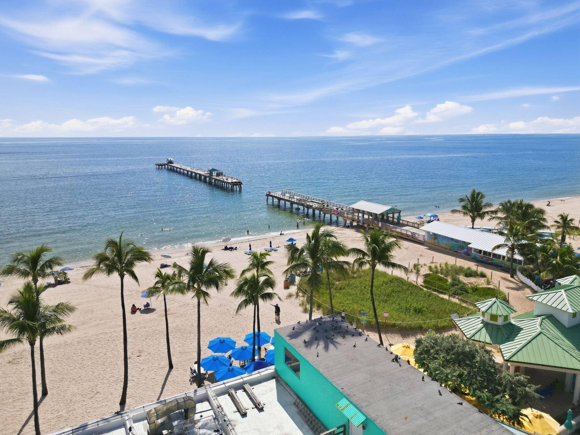 Expansive oceanfront with sandy beach, two piers, and palm trees