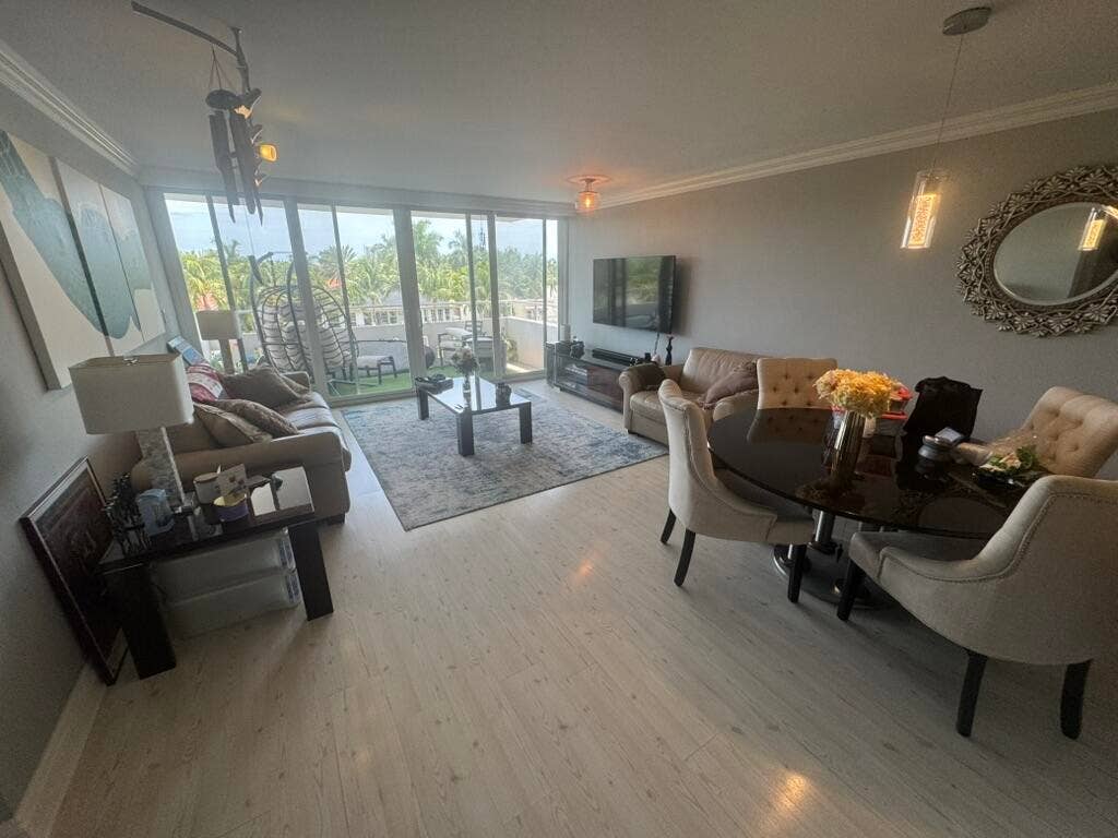 180 Isle Of Venice Drive, #433, Fort Lauderdale, FL 33301 Light wood-finish flooring extending throughout, spacious living area with crown molding, glass sliding doors leading to an outdoor balcony, built-in recessed lighting, and a modern dining area with an oval-shaped table