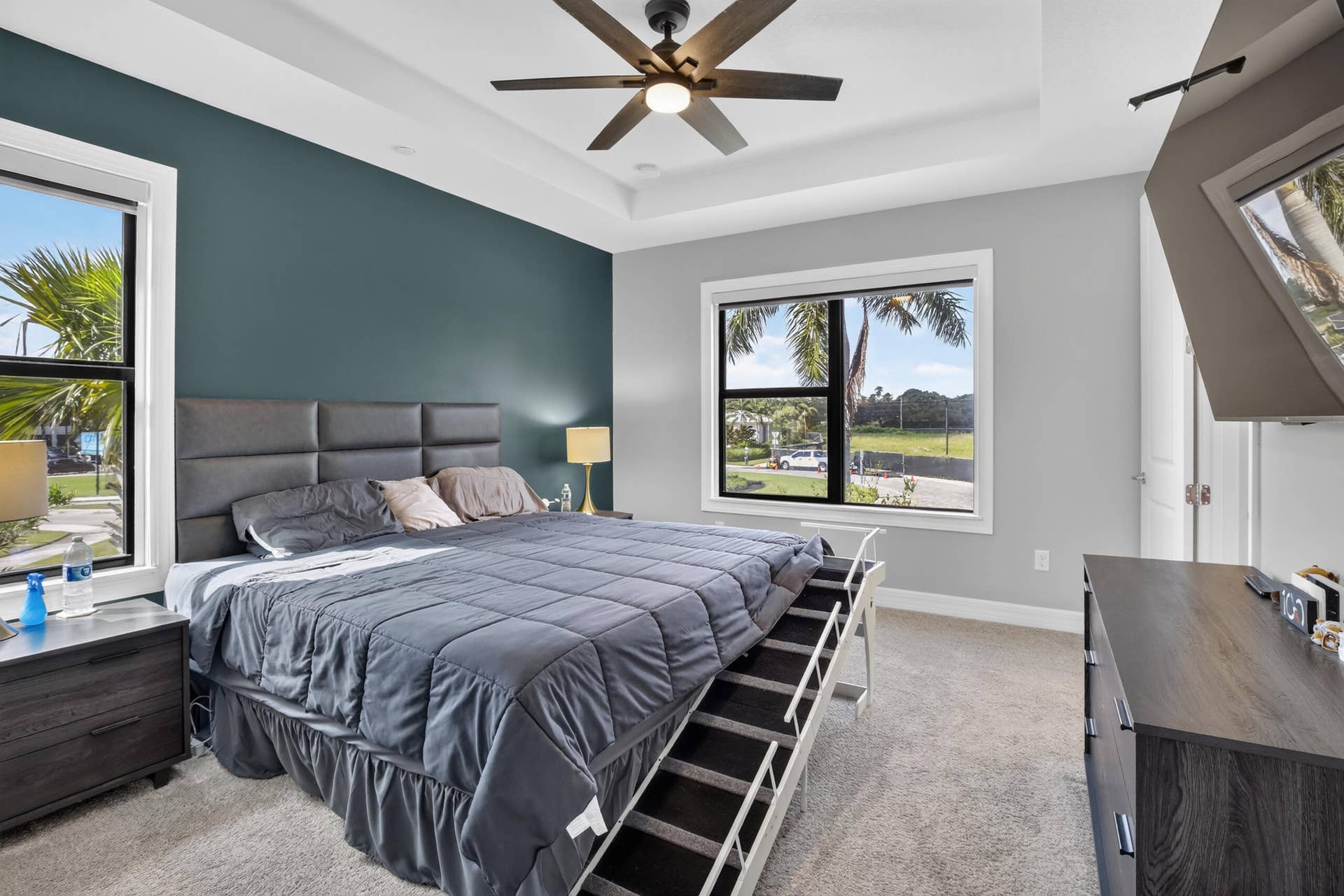 765 NW 84TH Terrace, Plantation, FL 33324 Primary bedroom suite featuring a tufted upholstered headboard, ceiling fan with brushed metal finish, and expansive windows overlooking manicured grounds