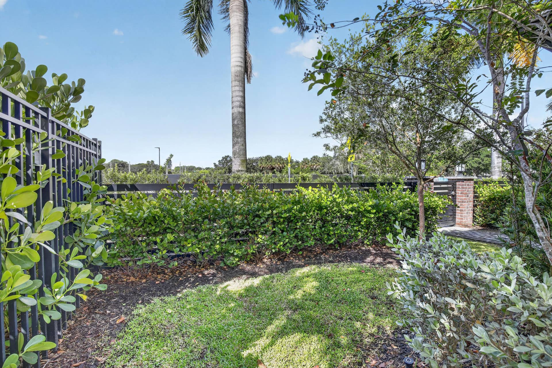 765 NW 84TH Terrace, Plantation, FL 33324 Mature landscaped grounds featuring a manicured lawn, lush perimeter hedging, decorative mulch beds, and established trees including a tall palm specimen