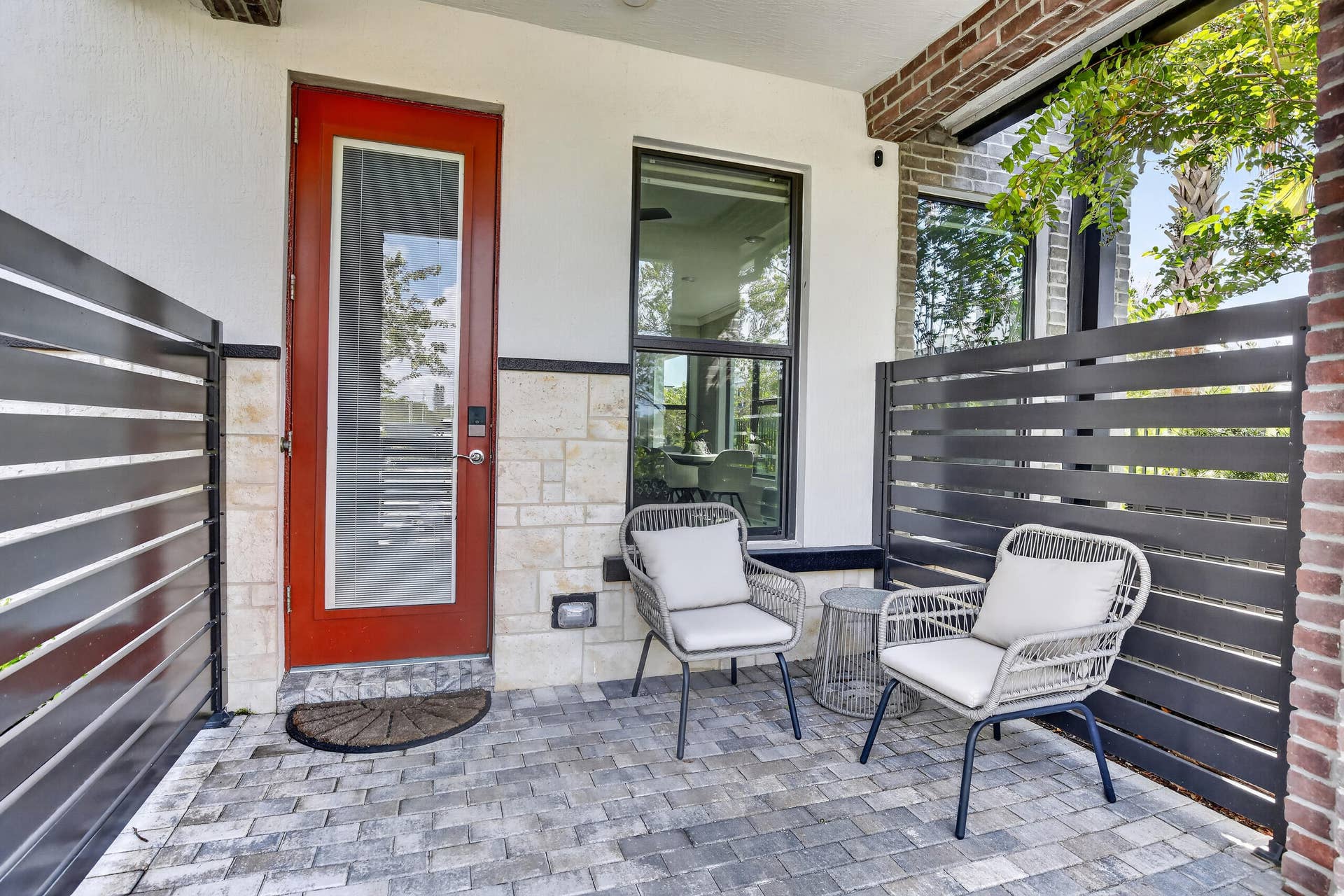 765 NW 84TH Terrace, Plantation, FL 33324 Welcoming front porch featuring a bold red entry door with sidelite window, horizontal slatted privacy screens, paver stone flooring, and comfortable seating areas ideal for outdoor relaxation