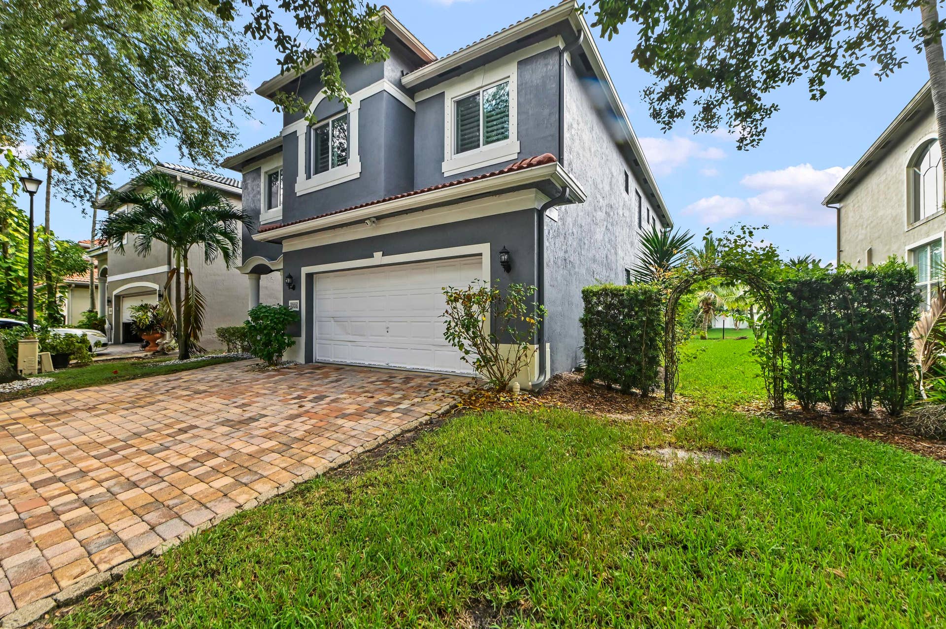 Two-story stucco exterior with white trim, a single garage, and a paver driveway