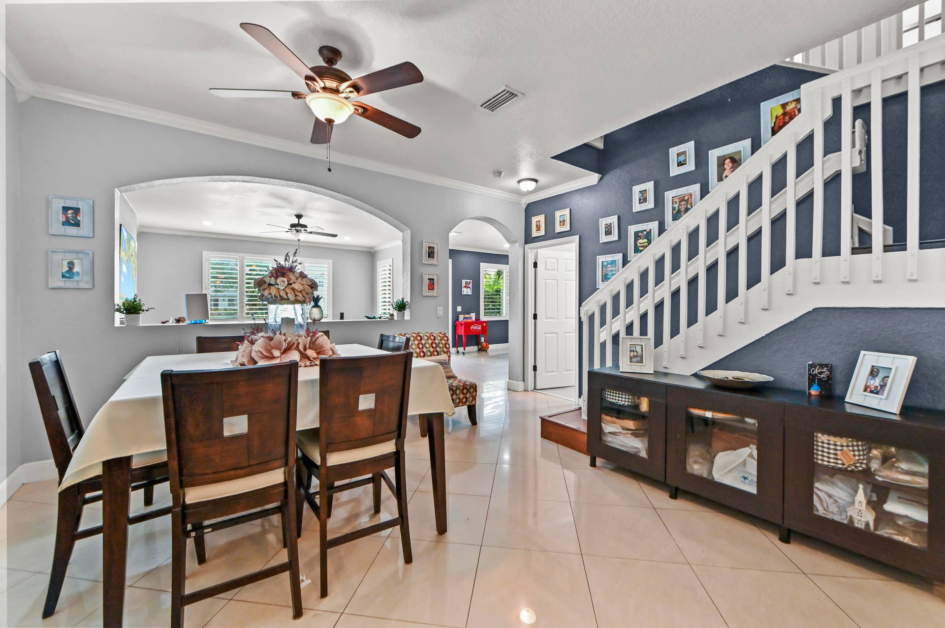 Tile flooring, arched pass-through window, ceiling fan, white balustrade, and built-in cabinetry