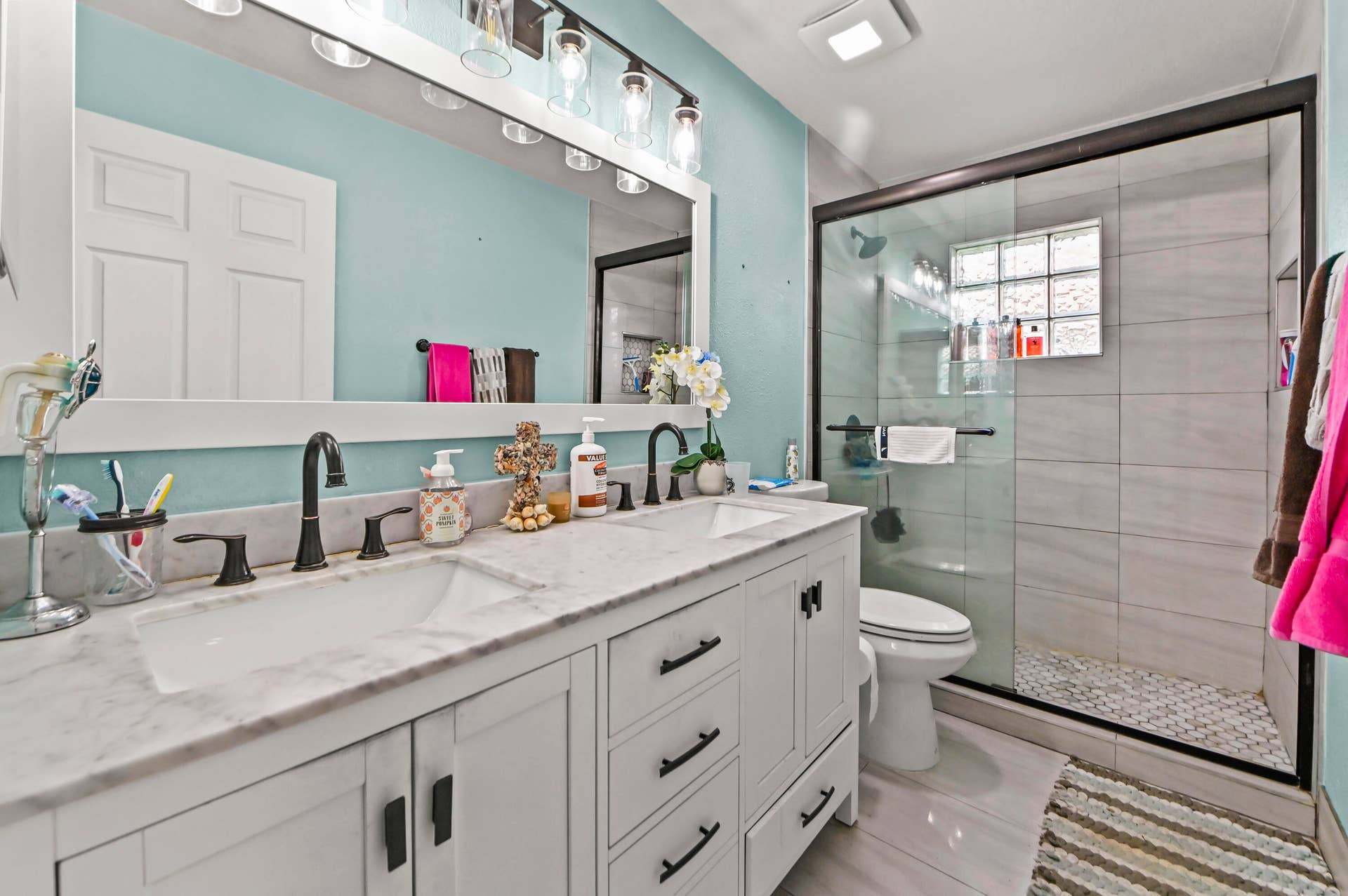 Spa-inspired primary bathroom featuring dual vanities with white cabinetry, marble-finish countertops, and matte black fixtures