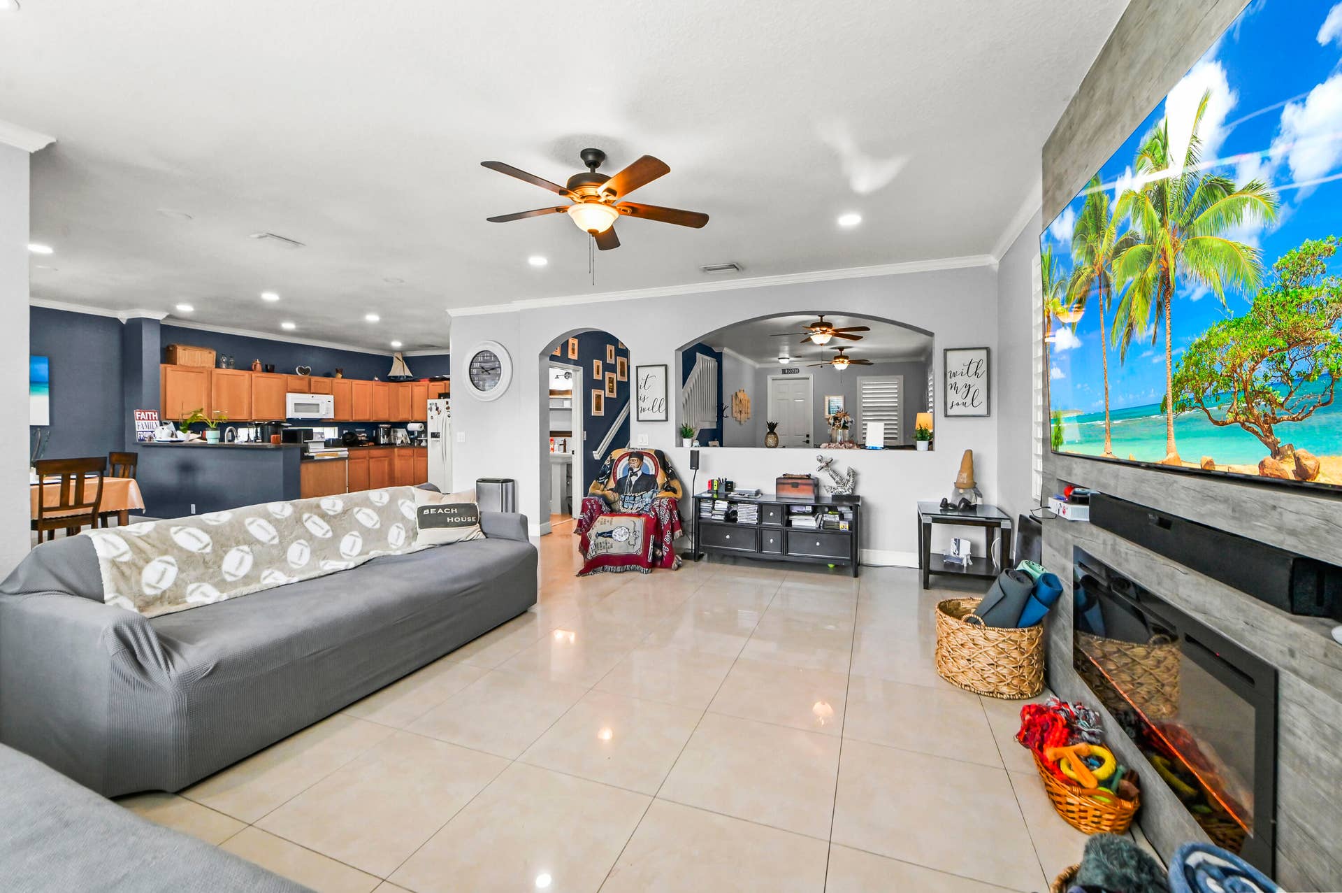 Open-concept living area featuring polished tile flooring, a ceiling fan with integrated lighting, and a wood-finish kitchen cabinetry with stainless steel appliances