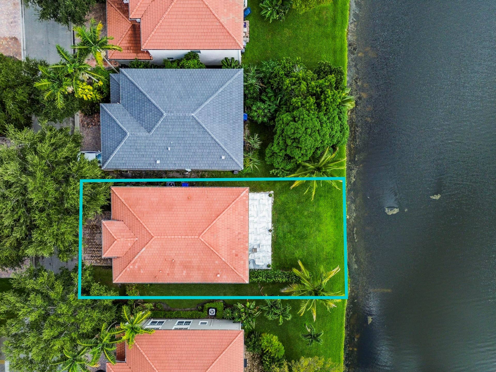 Waterfront property featuring a red tile roof, expansive green lawn, and a light-colored patio