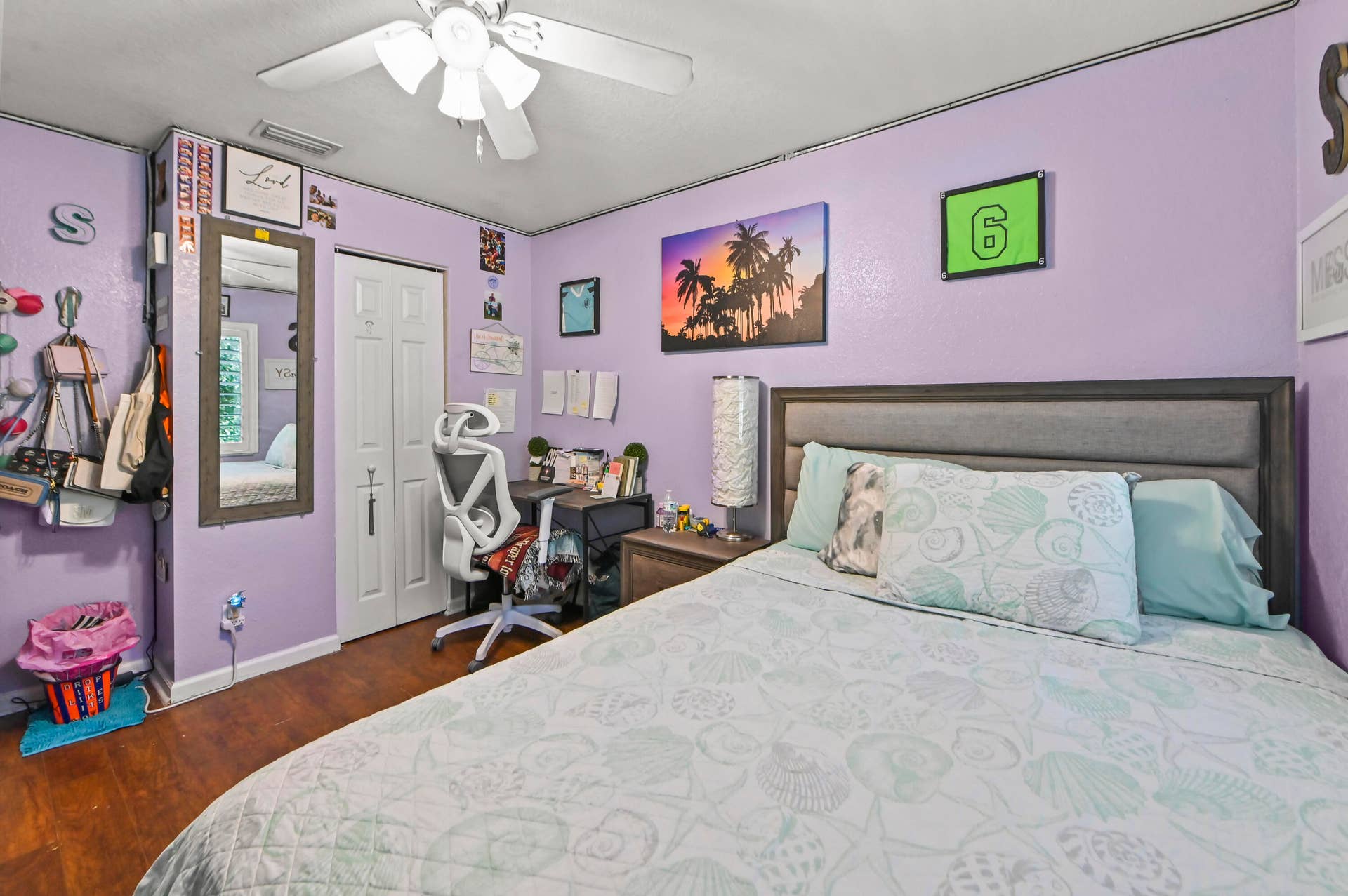 Spacious bedroom featuring a wood-finish floor, purple accent walls, and a gray upholstered bed frame
