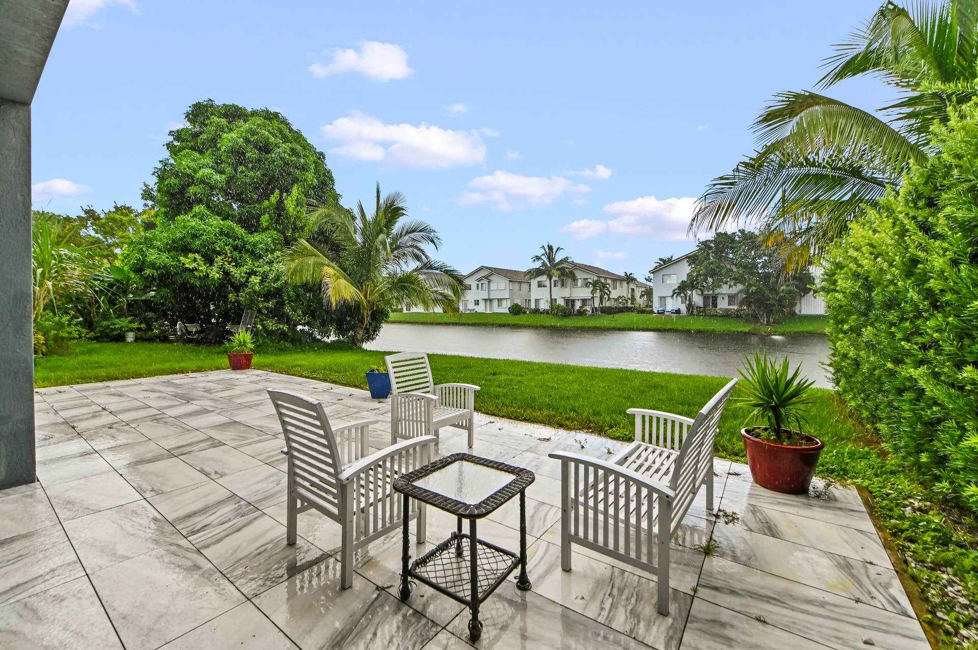 Expansive patio with large format paver tiles, mature tropical landscaping, and water frontage