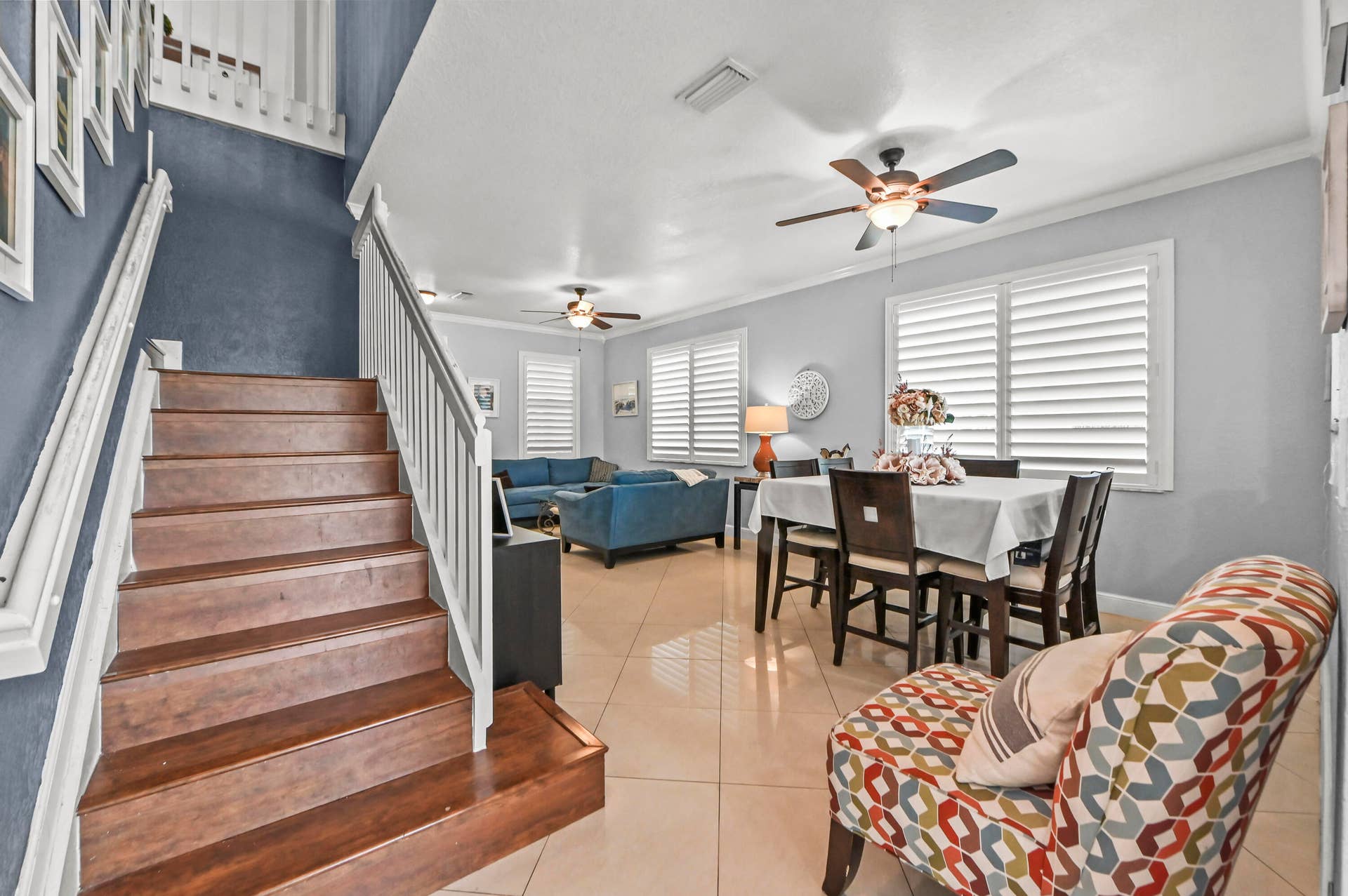 Wood-finish staircase with white railings, tile flooring, and multiple ceiling fans