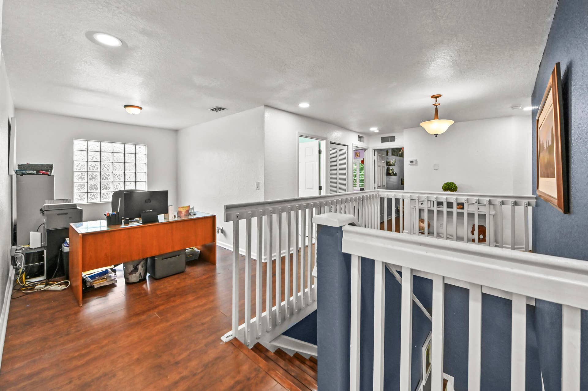 Spacious open loft area with wood-finish flooring, recessed lighting, and a glass block window
