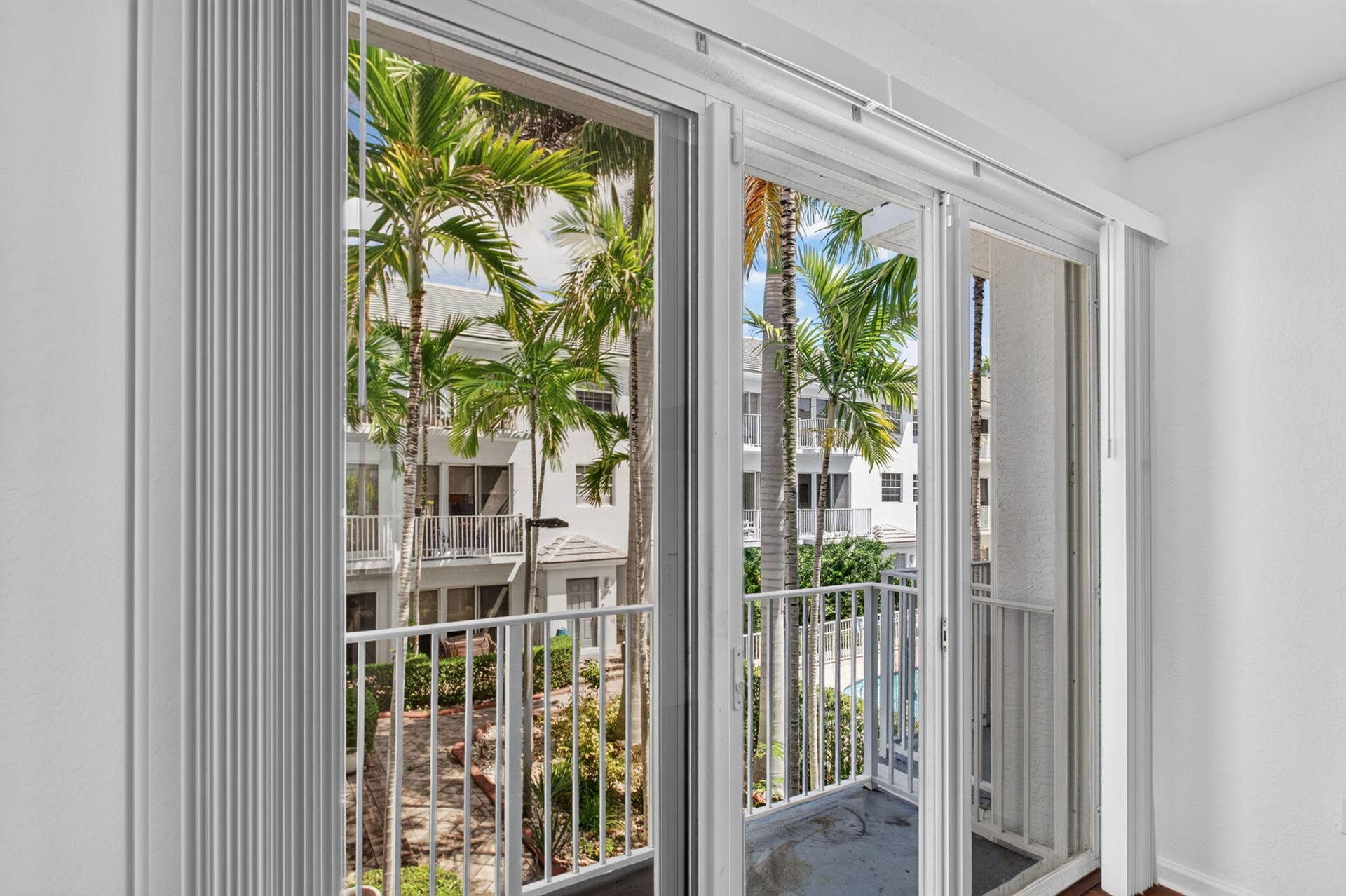 2725 NE 8TH Avenue, #112, Wilton Manors, FL 33334 Sliding glass doors with vertical blinds open to a private balcony with a white metal railing