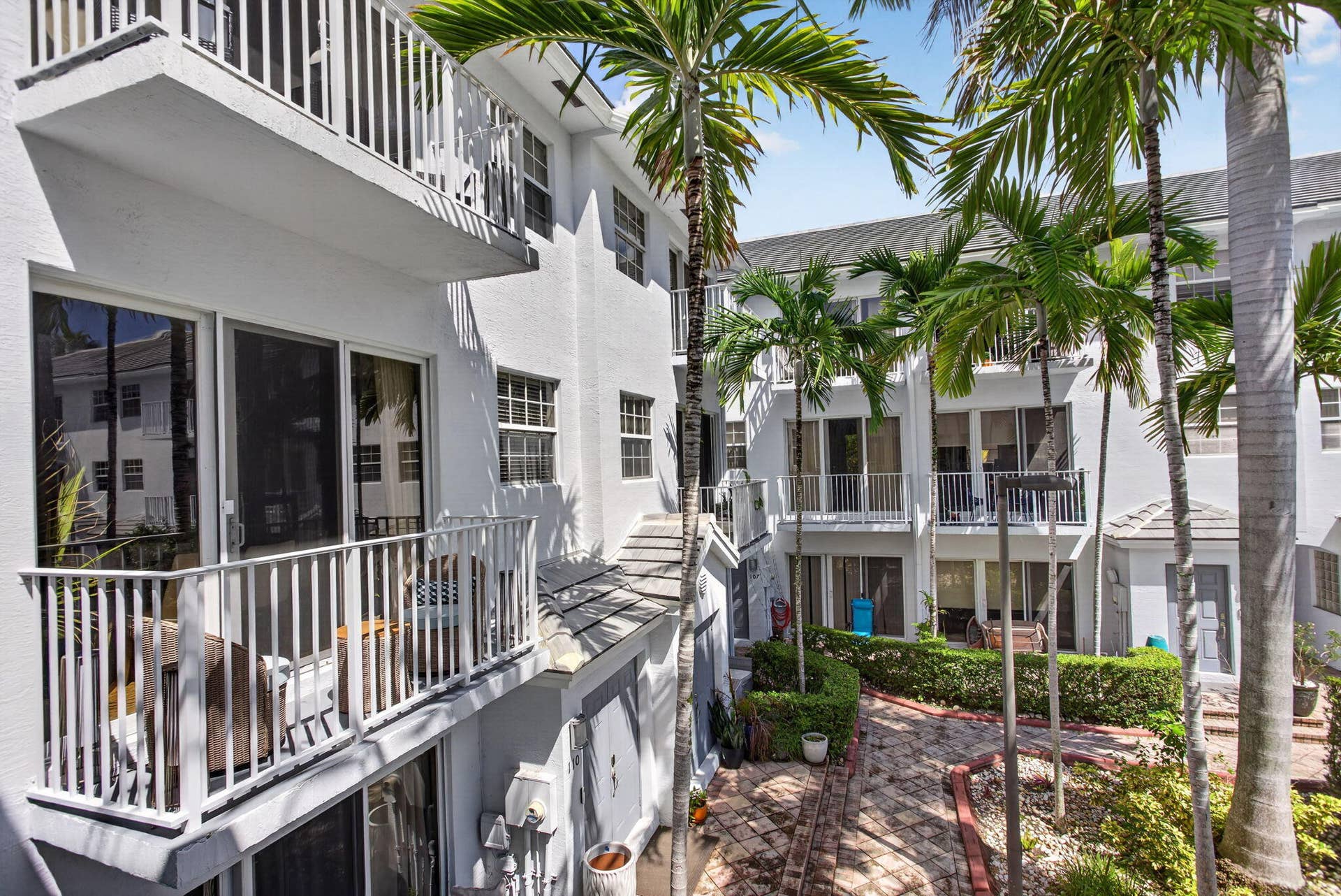 2725 NE 8TH Avenue, #112, Wilton Manors, FL 33334 White stucco exterior with multiple balconies, sliding glass doors, and mature palm trees
