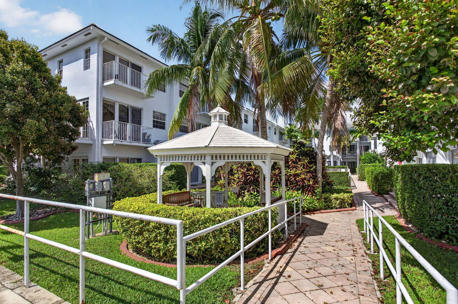 2725 NE 8TH Avenue, #112, Wilton Manors, FL 33334 Multi-level building with individual balconies, white gazebo, paved pathway, manicured hedges, and mature palm trees