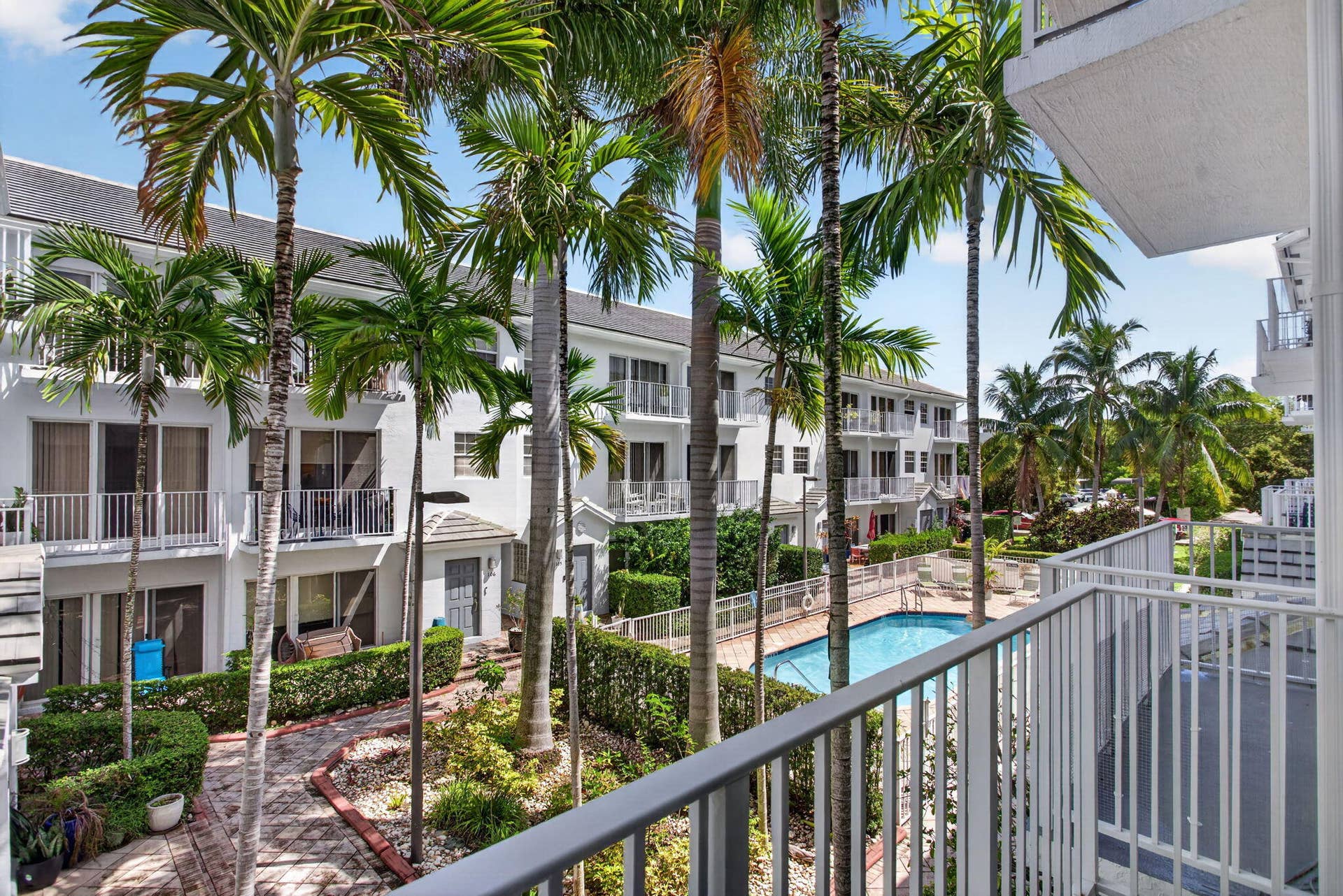 2725 NE 8TH Avenue, #112, Wilton Manors, FL 33334 Balcony overlooking courtyard with palm trees, swimming pool, and multiple-story residential buildings