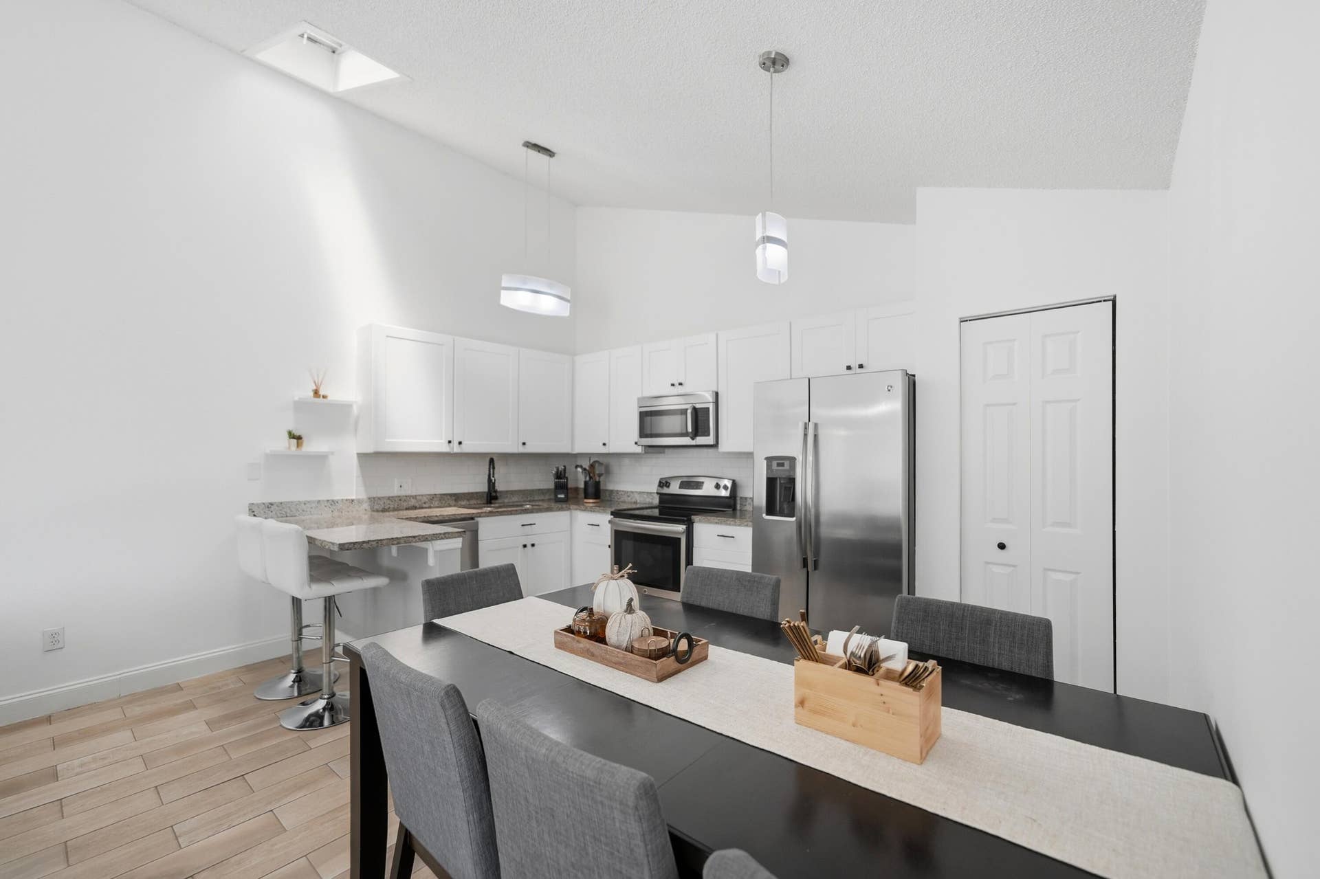 Vaulted ceiling with skylight, white shaker cabinetry, stainless steel appliances, granite countertops, and wood-finish flooring
