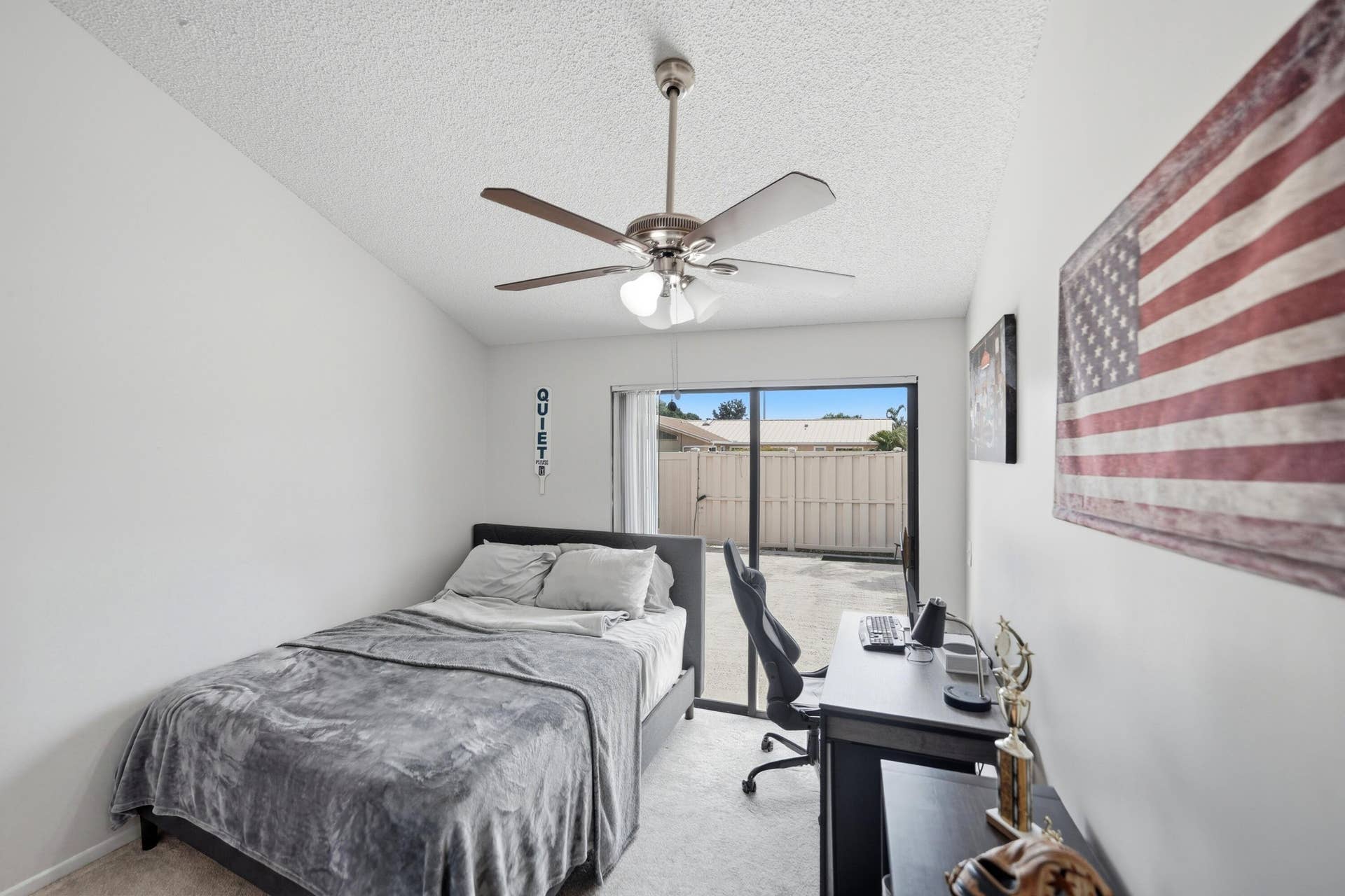 Textured ceiling with a ceiling fan light fixture, sliding glass door, and a private outdoor patio