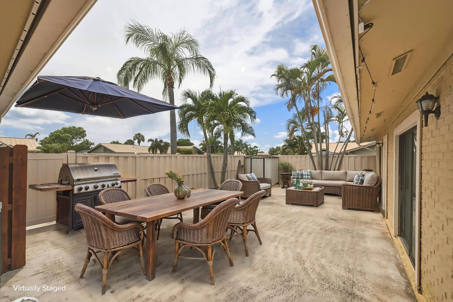 Expansive concrete patio with a privacy fence, exterior lighting, and mature palm trees
