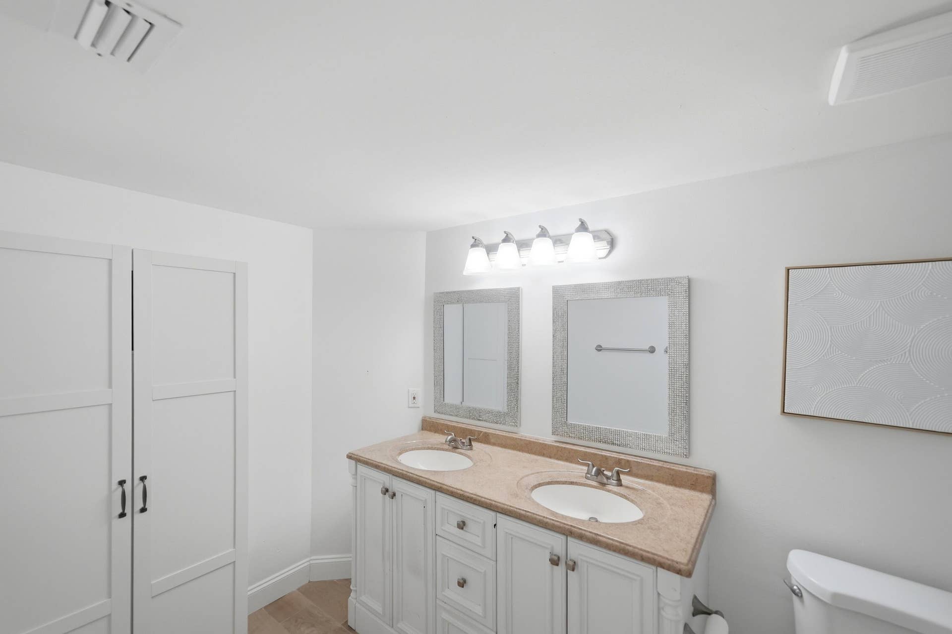 Spa-inspired primary bathroom featuring dual vanities with wood-finish countertops, white cabinetry with hardware accents, and polished chrome fixtures