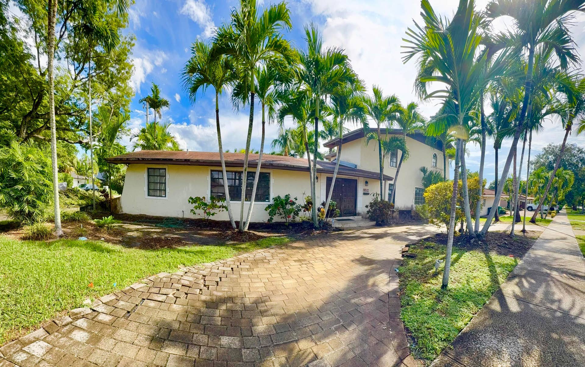 2390 NE 199th Street, Aventura, FL 33180 Stucco exterior residence featuring a paver driveway, mature palm trees, and a sidewalk border