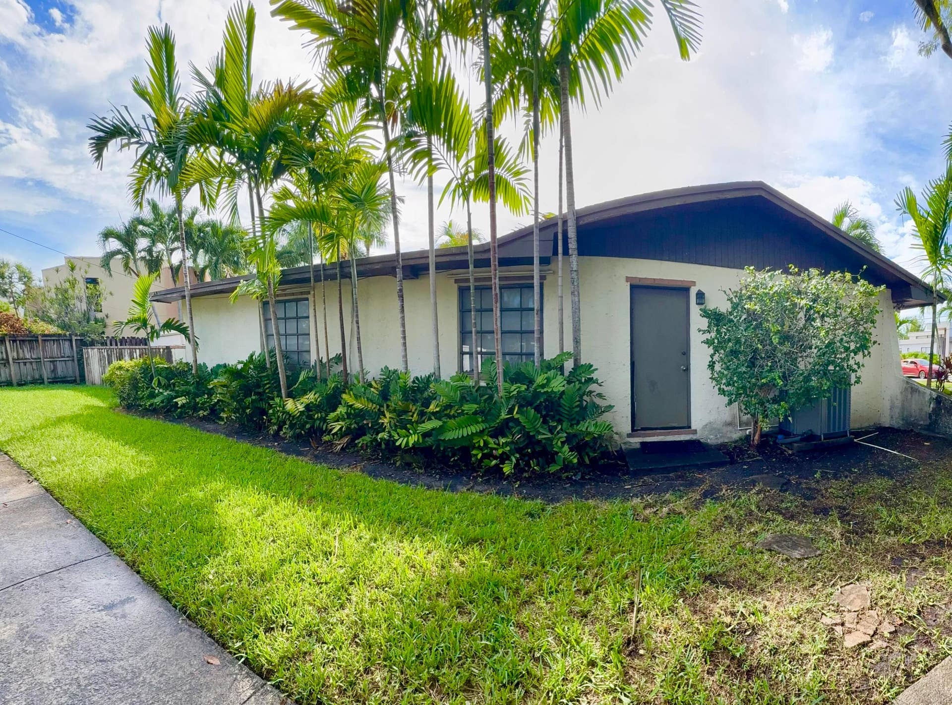 2390 NE 199th Street, Aventura, FL 33180 Exterior featuring a stucco finish, multiple palm trees, and a landscaped planting bed