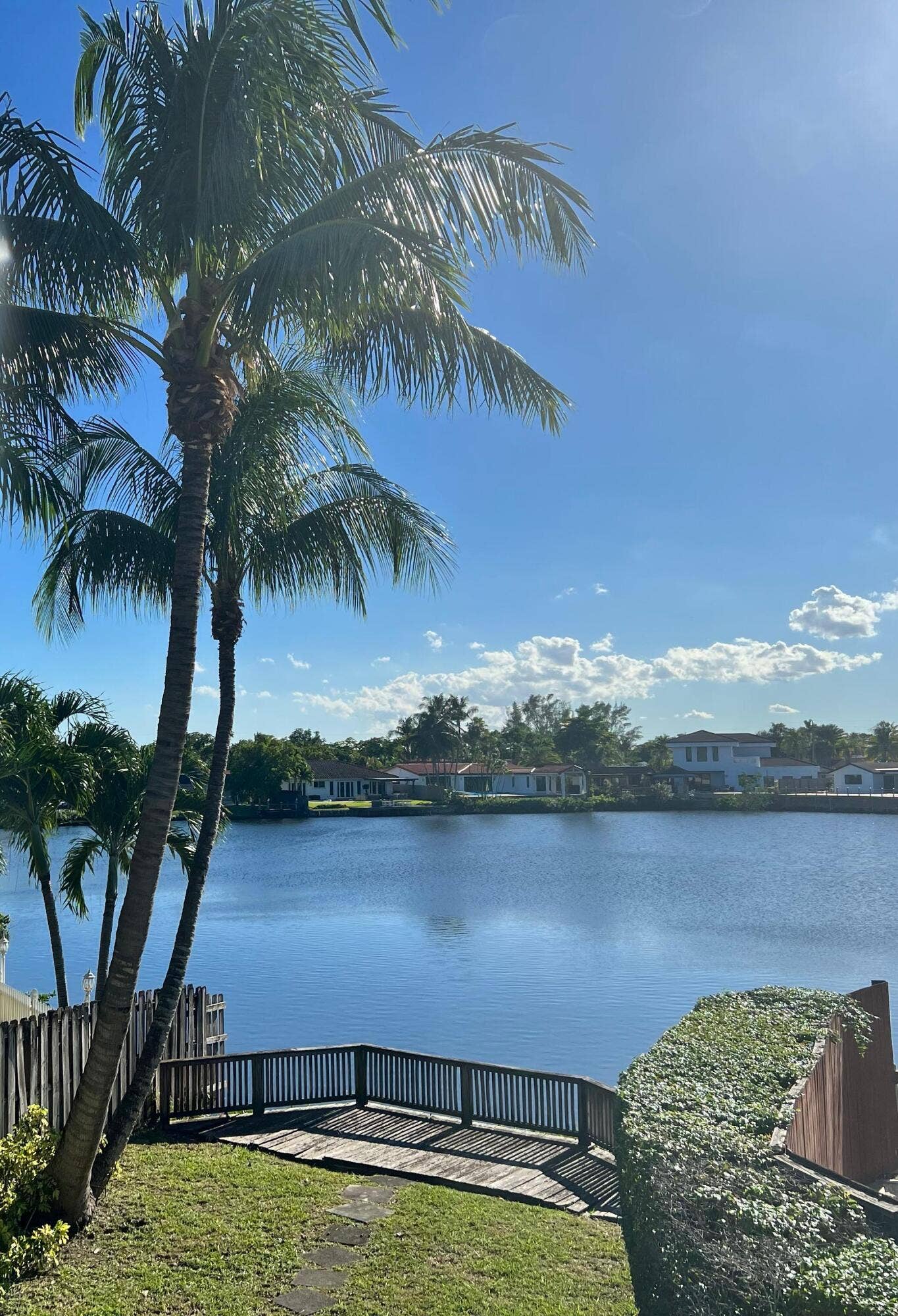 2390 NE 199th Street, Aventura, FL 33180 Waterfront property featuring a wood deck, mature palm trees, and lush landscaping