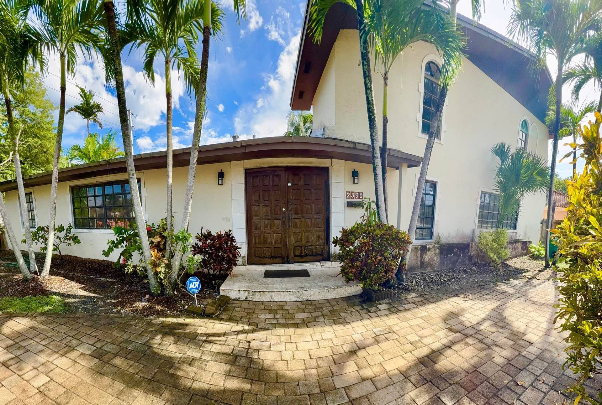2390 NE 199th Street, Aventura, FL 33180 Stucco exterior with a paver driveway, double wood-finish entry doors, and arched windows