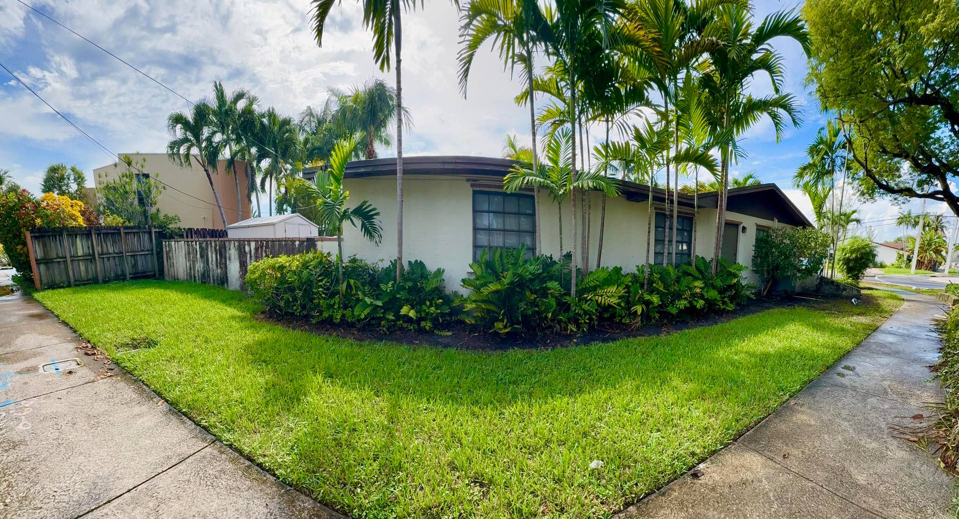 2390 NE 199th Street, Aventura, FL 33180 Corner lot property featuring exterior landscaping with palm trees and shrubs, a stucco exterior, and a wooden fence