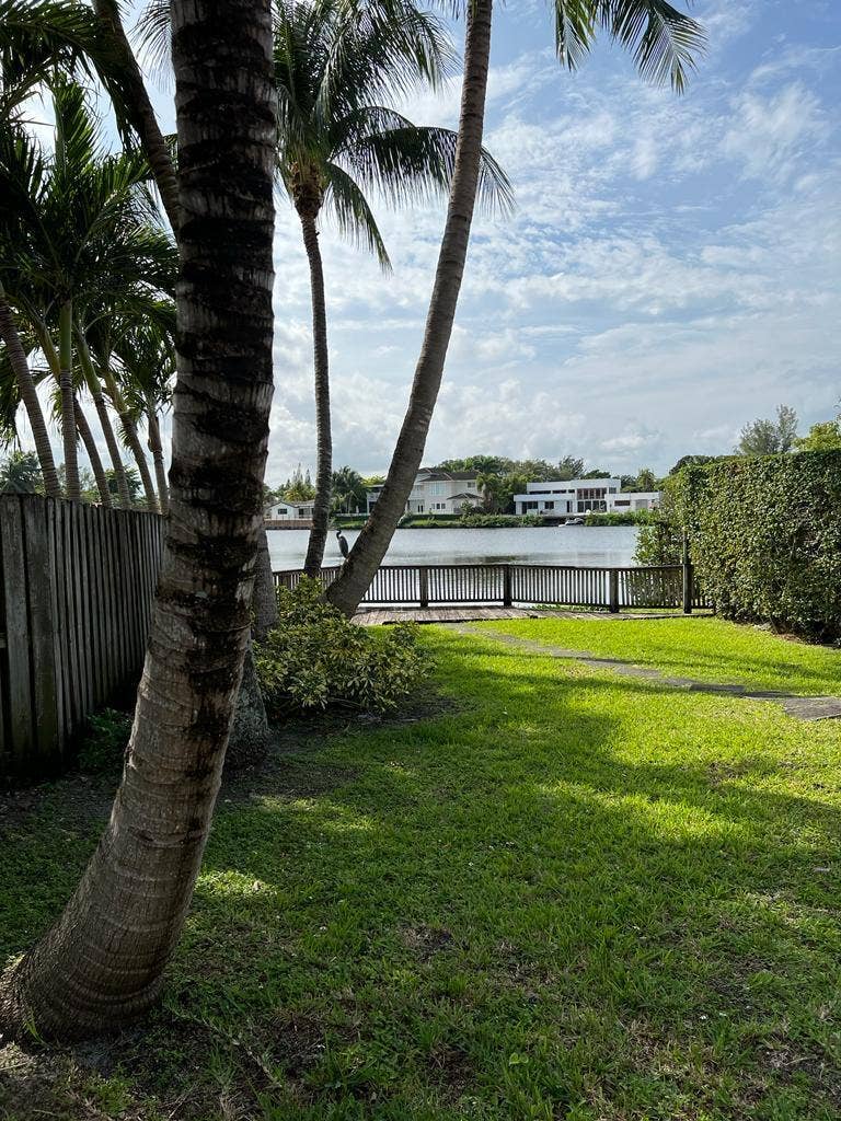 2390 NE 199th Street, Aventura, FL 33180 Expansive green space featuring a wooden fence, mature palm trees, and waterfront access with a dock