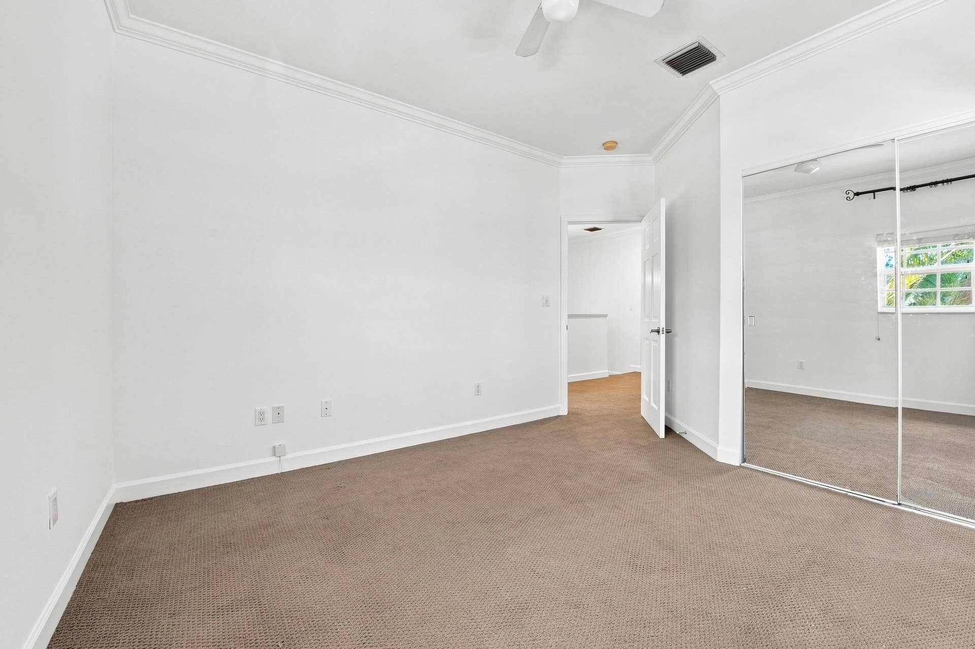 Spacious bedroom featuring neutral wall finishes, neutral carpeting throughout, mirrored closet doors, and abundant natural light from multiple windows