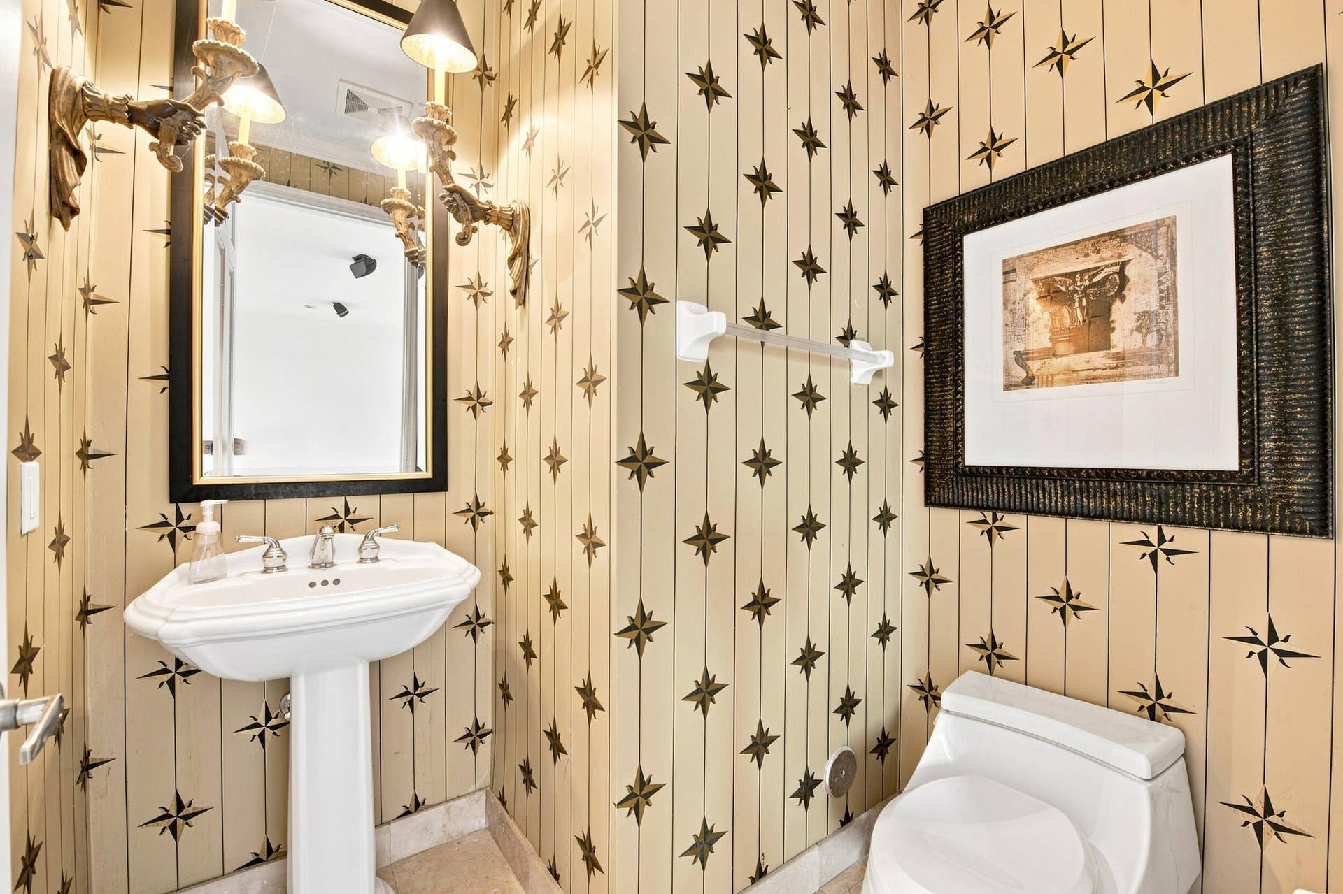 Pedestal sink with polished chrome faucet, framed mirror, and wall-mounted sconce lighting