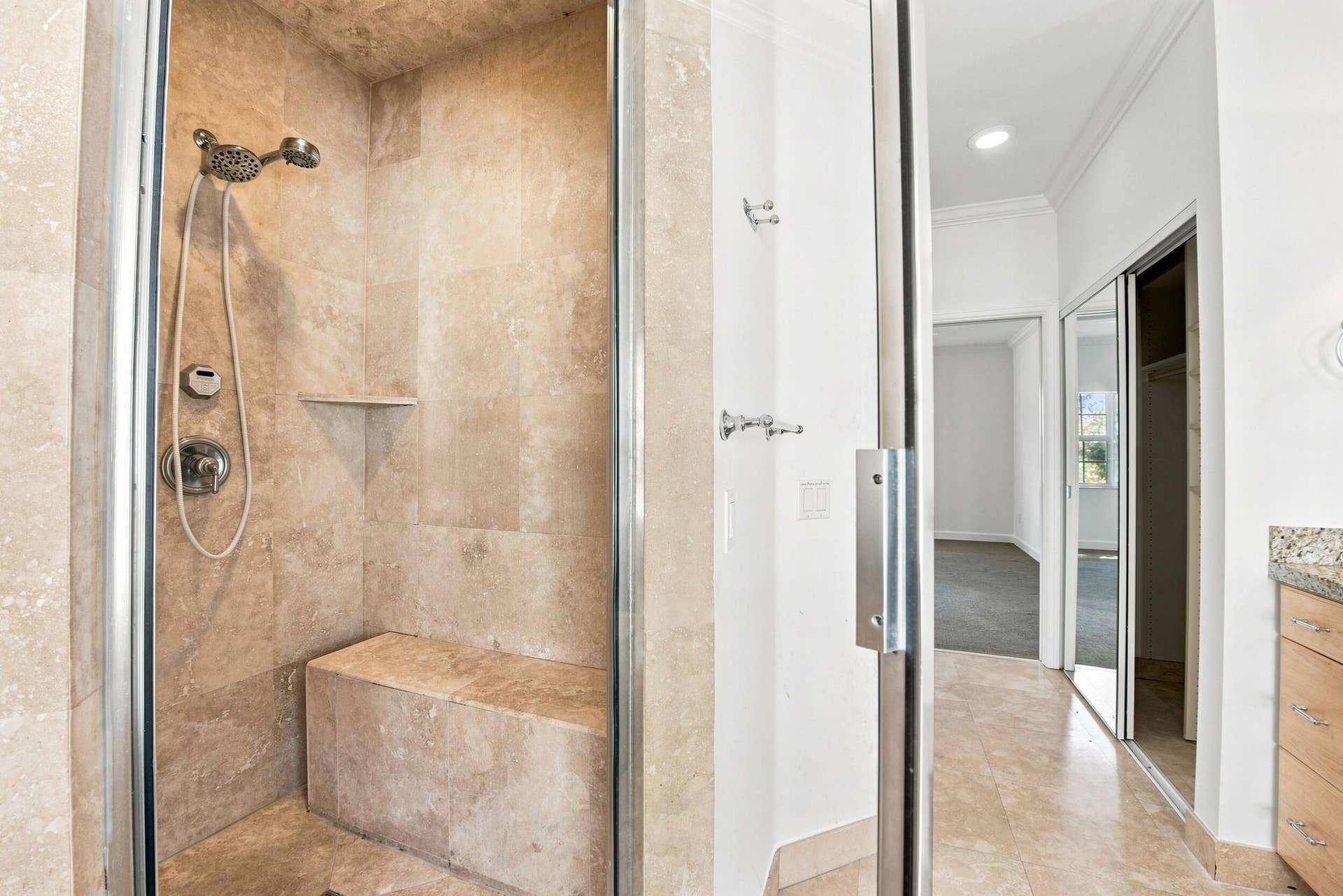 Glass-enclosed shower with a built-in bench, corner shelf, and polished chrome fixtures