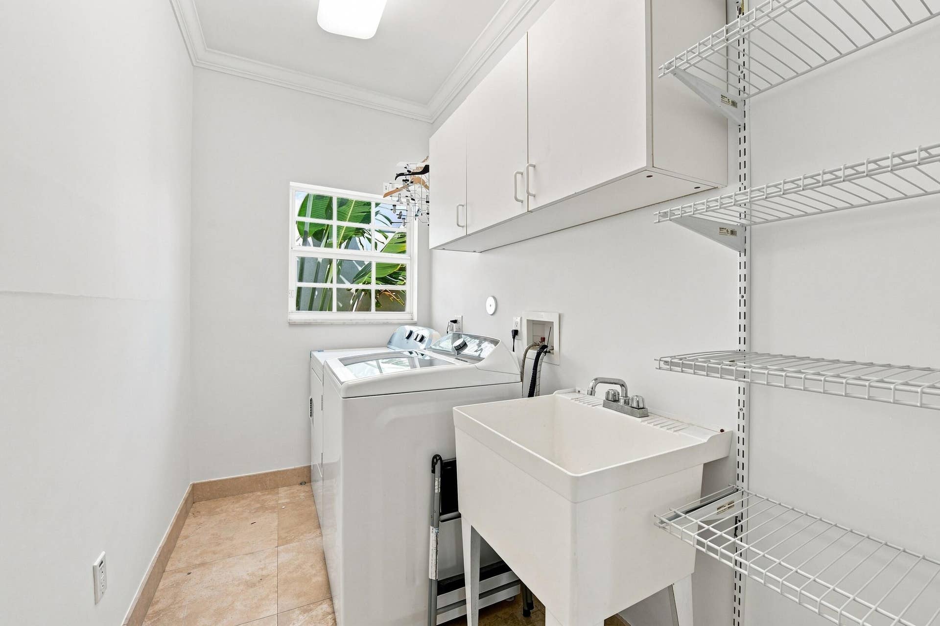 Utility room featuring tile flooring, a window, upper cabinetry, a laundry sink, and wire shelving