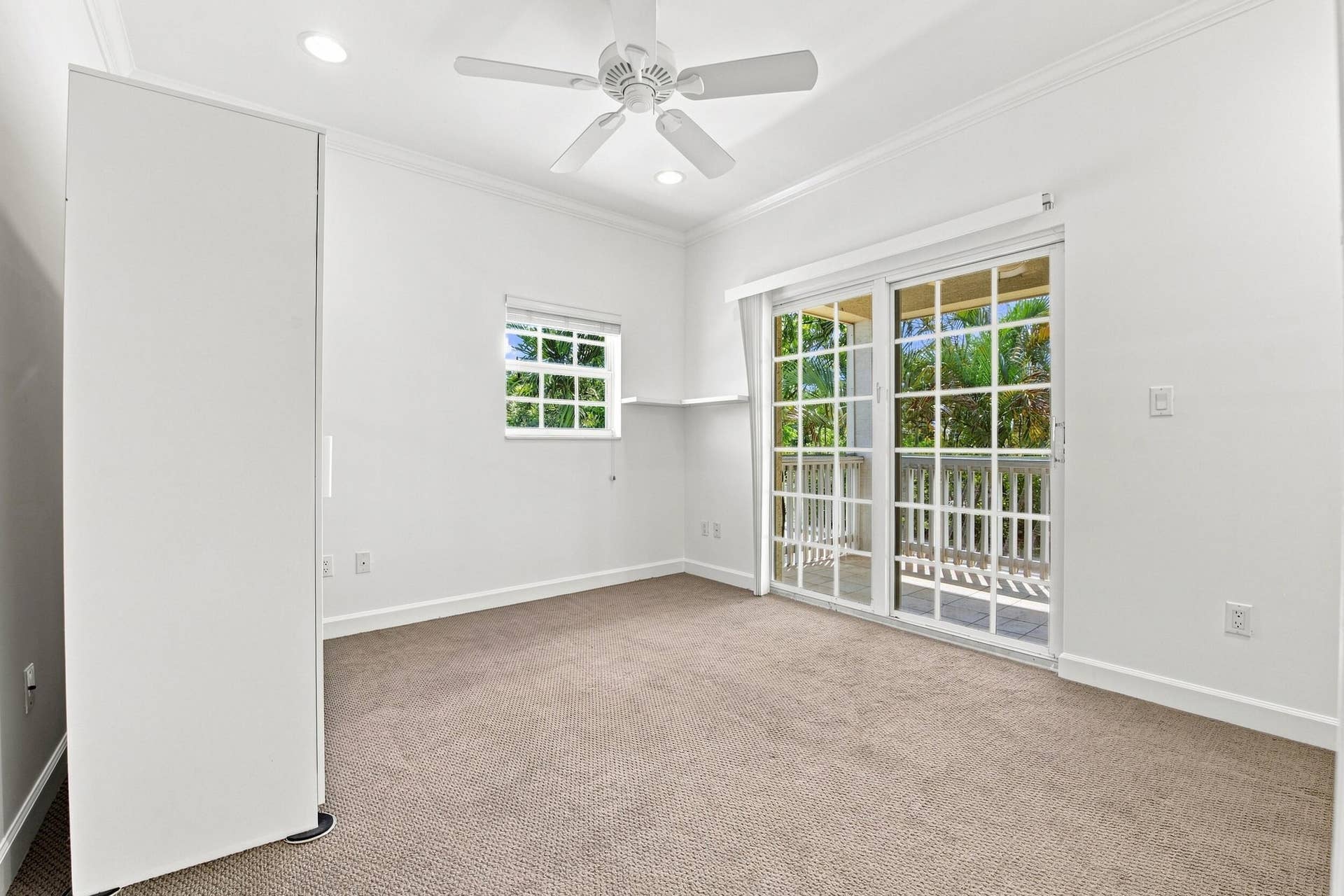 Neutral tone carpeting, crown molding, a built-in wardrobe, and a ceiling fan with light fixture