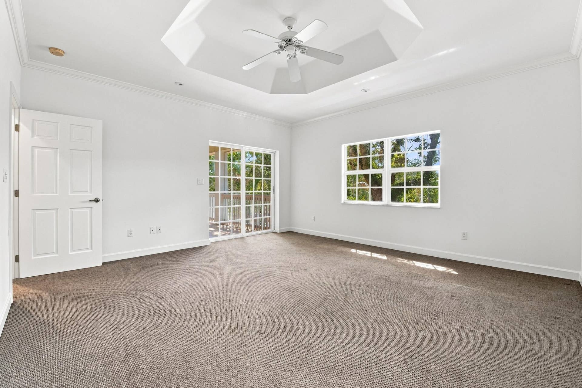 Tray ceiling with ceiling fan, white paneled door, sliding glass door, large window, and carpeted flooring