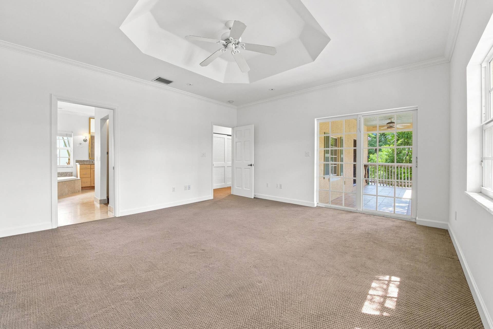 Tray ceiling with a ceiling fan, white crown molding, and sliding glass doors leading to an outdoor space
