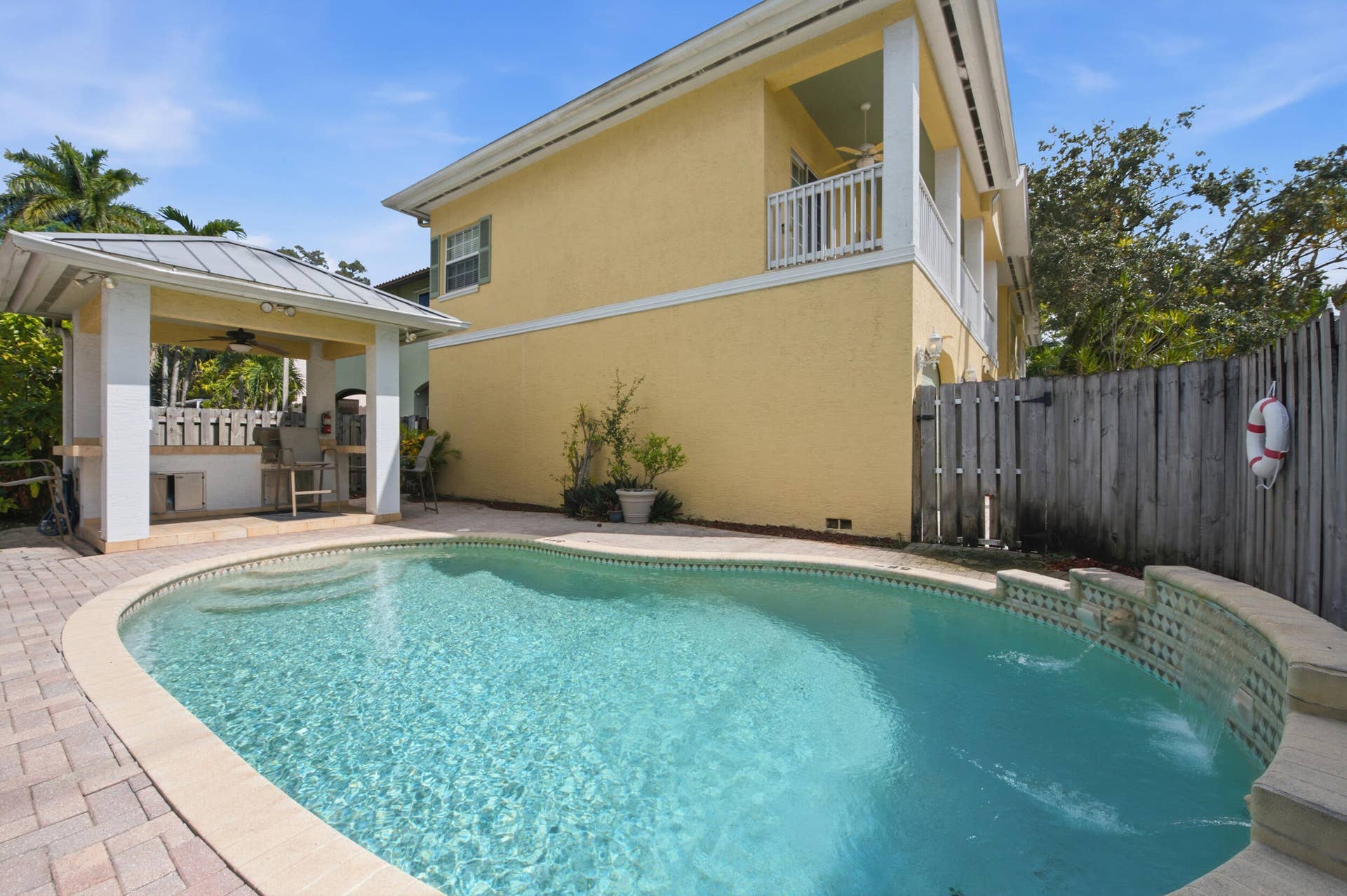 Outdoor oasis featuring a curved swimming pool, integrated spa with water features, a covered outdoor kitchen, and a second-story balcony