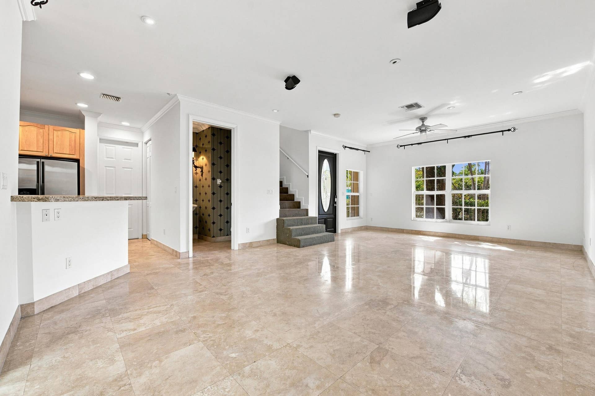Spacious open-concept living area featuring polished stone-finish flooring throughout, recessed ceiling lighting, and a ceiling fan