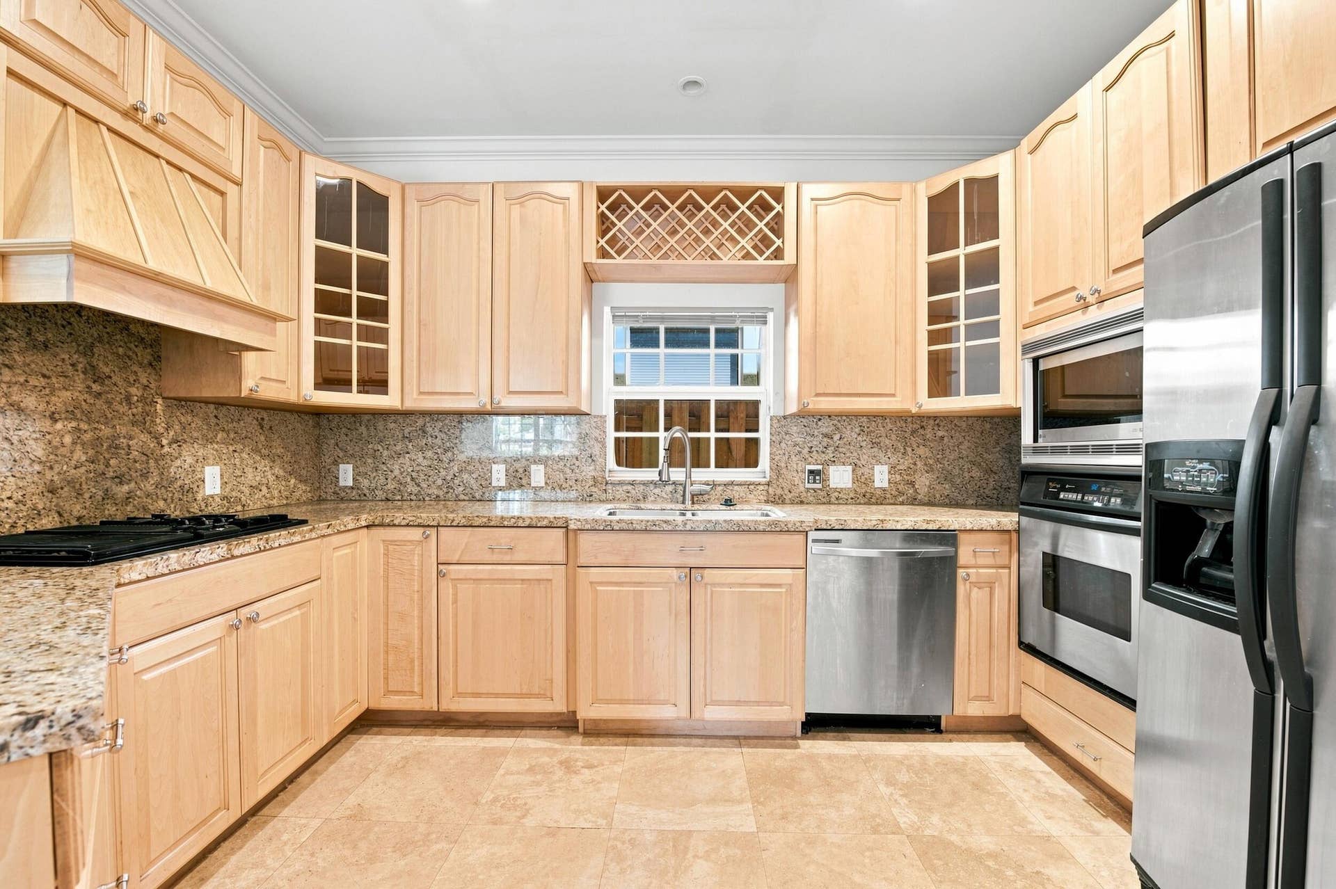 Light-toned wood cabinetry with glass-front accents, granite countertops, tile flooring, stainless steel appliances, and a built-in wine rack