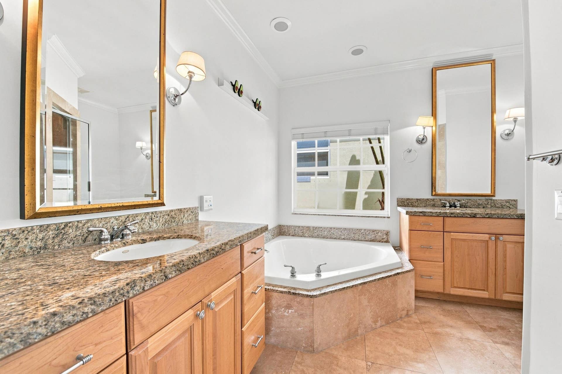 Dual vanity with granite countertops, light wood-finish cabinetry, a built-in corner soaking tub, and tiled flooring