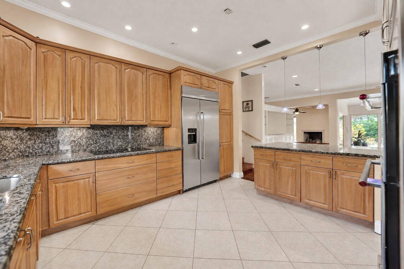 Ceramic tile flooring, light wood-finish cabinetry, stainless steel refrigerator, granite countertops, and recessed lighting. Wall color has been virtually enhanced.