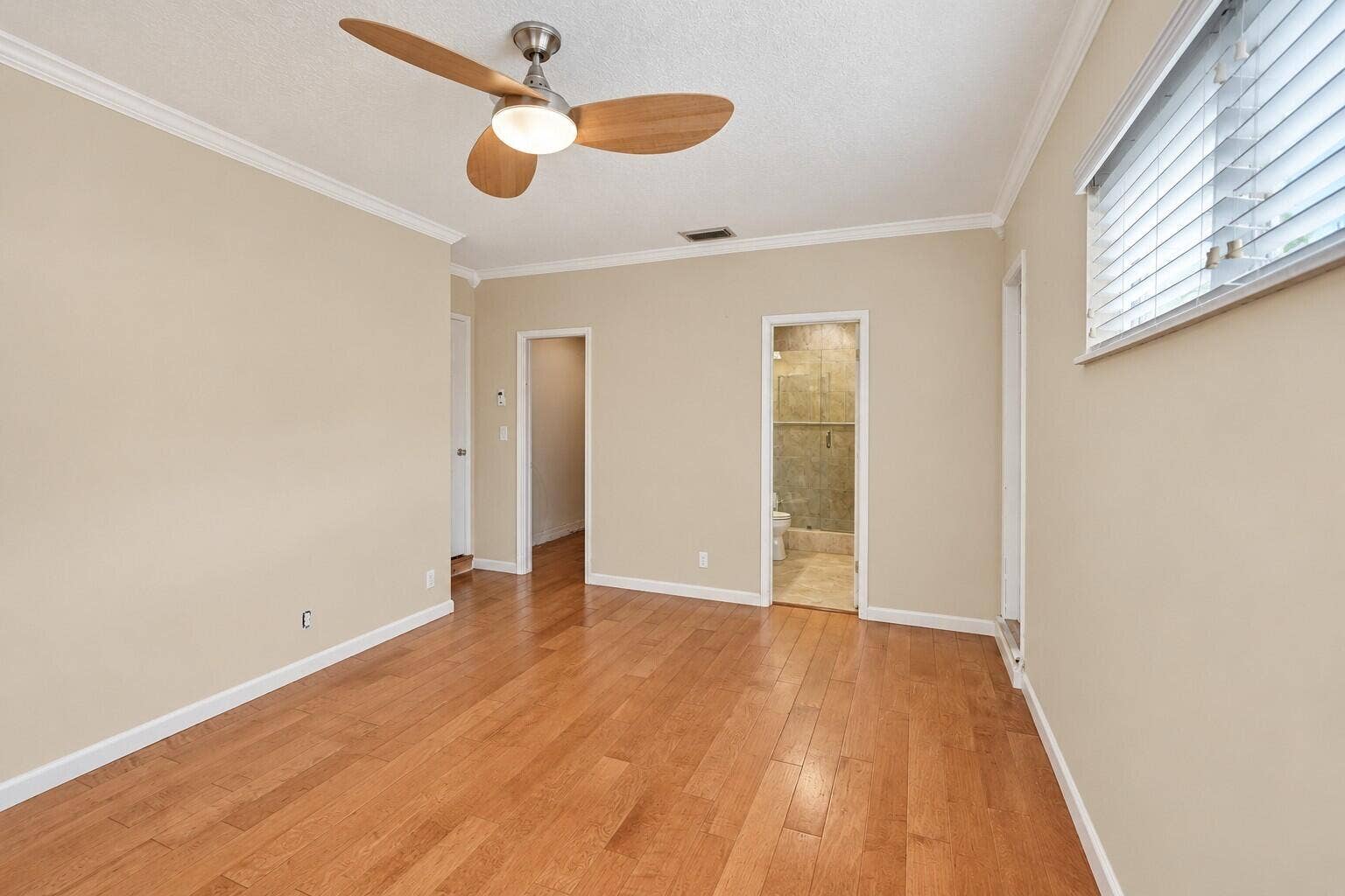 Wood-finish flooring with neutral wall tones, crown molding, and a ceiling fan with integrated lighting