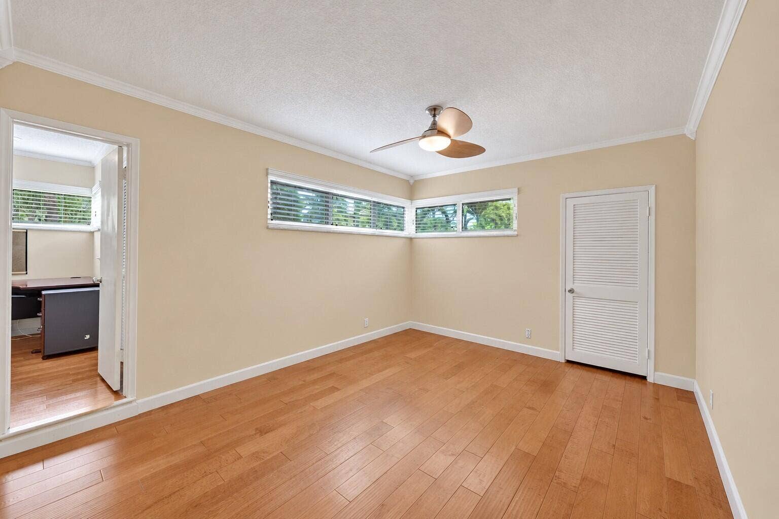 Wood-finish flooring with crown molding, transom-style windows, and a ceiling fan